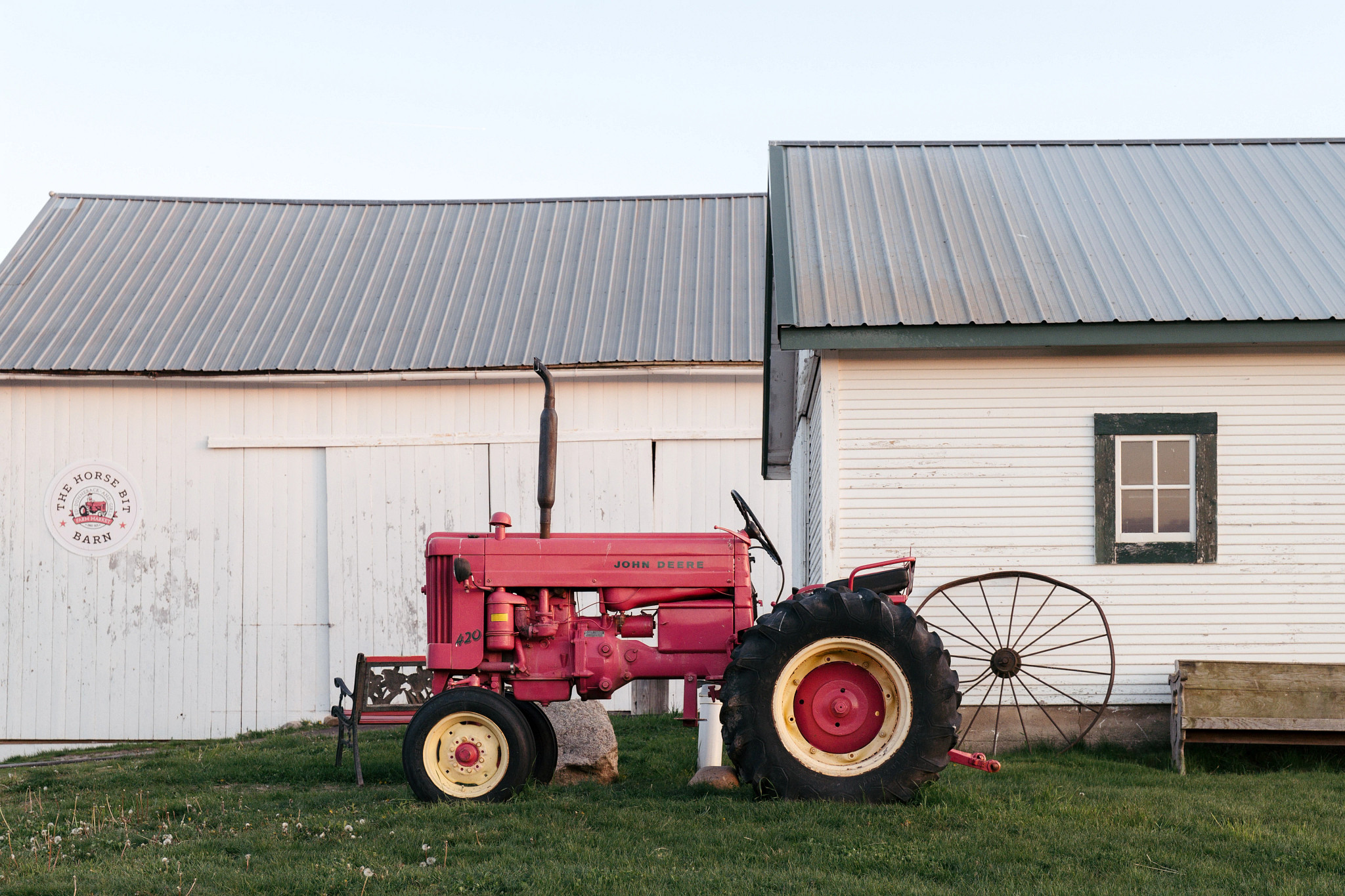 A pink vintage tractor parked next to a white barn in a rural setting