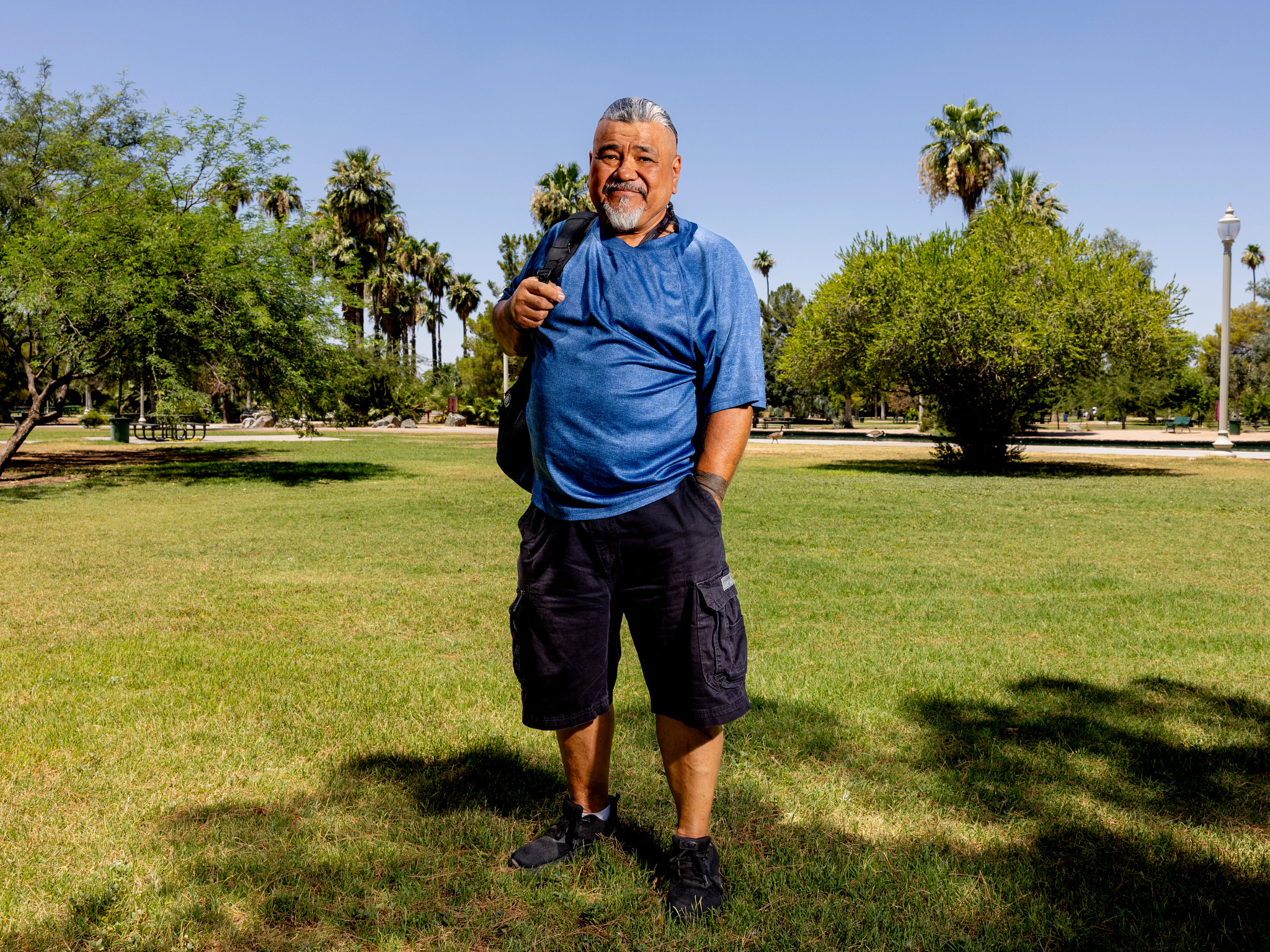 a man stands in a park with a backpack slung over one shoulder
