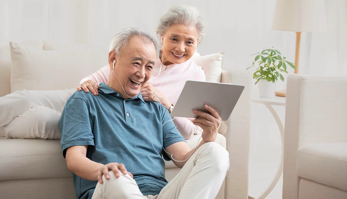 Mature couple sitting on the couch in their living room and listening to SingFit on headphones