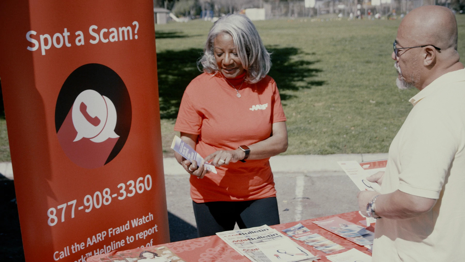 an a a r p volunteer at a scam prevention event shows a visitor a pamphlet