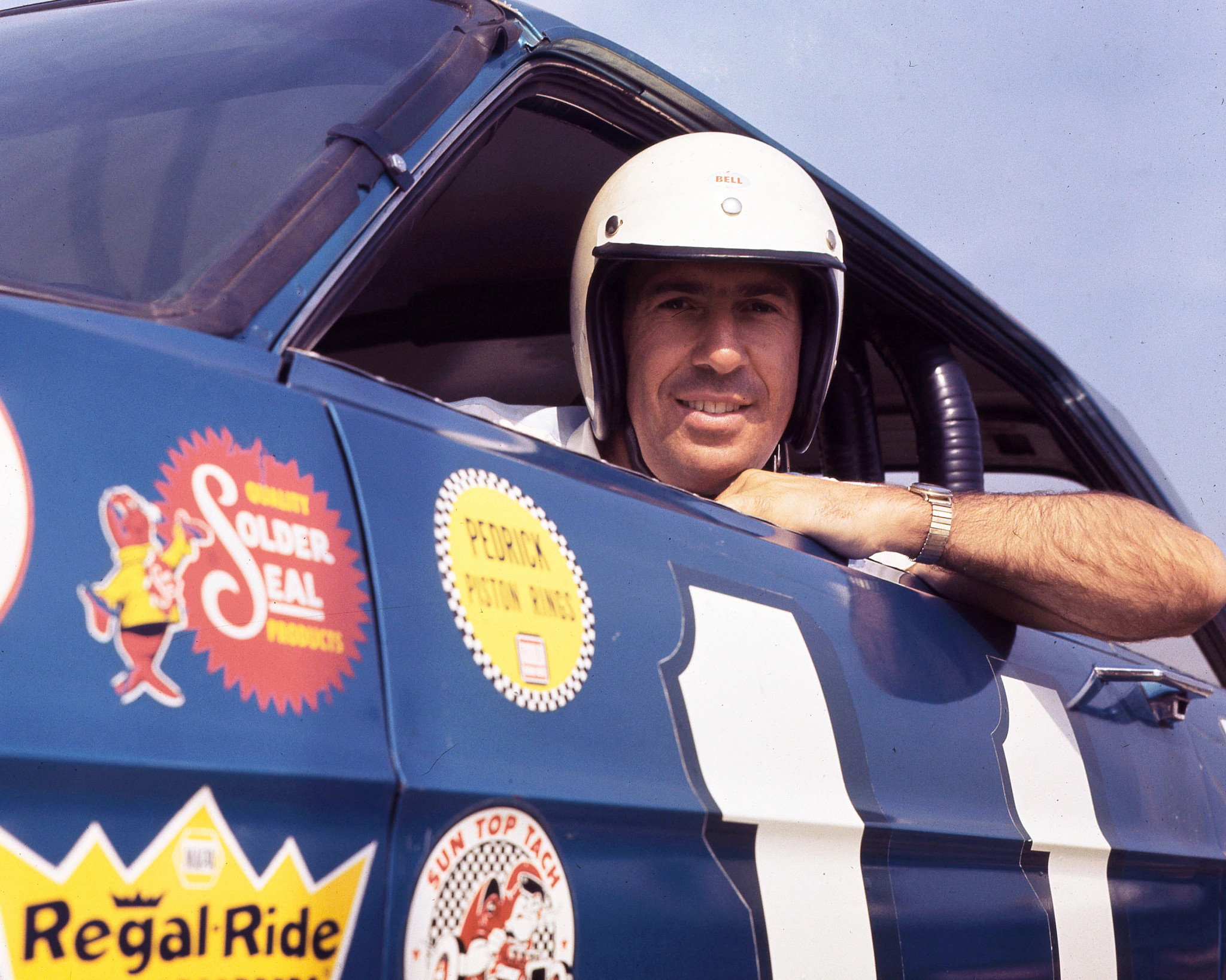 ned jarrett in his racing helmet sitting in a race car and smiling
