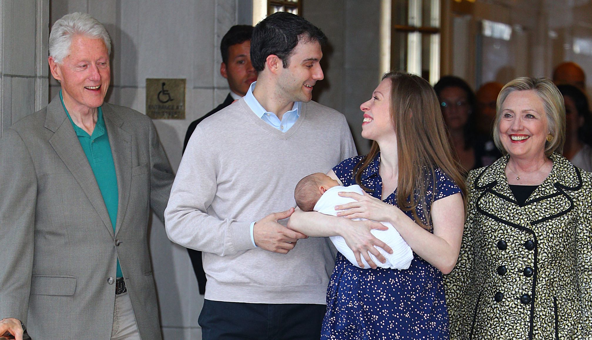 Chelea, Bill and Hillary Clinton chelsea clinton looks up at her husband while holding her newborn baby in her arms. parents bill and hillary clinton stand behind them.