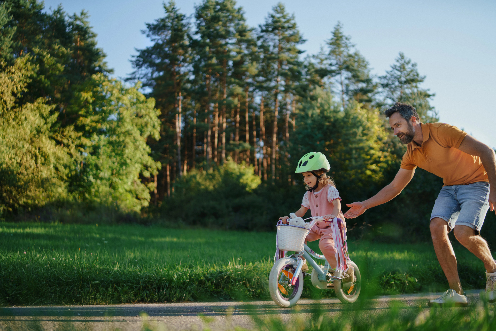 Little girl in cycling helmet getting support from her father when riding bike for the first time.