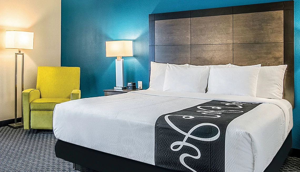 La Quinta® by Wyndham hotel bed with white linens and black throw blanket against blue wall