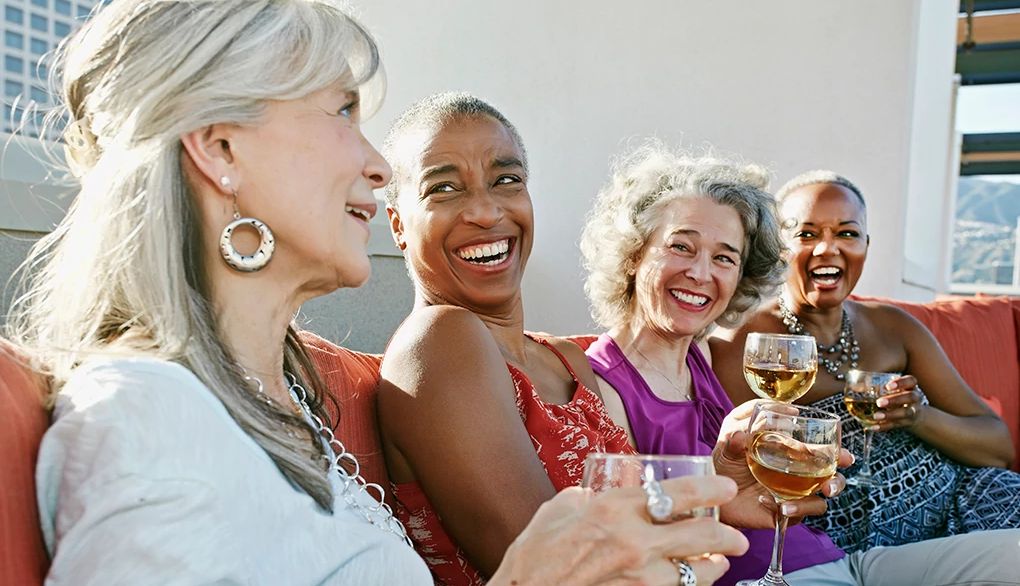 Humans are social beings, wired to connect with others Four women drinking wine together on a couch on a rooftop