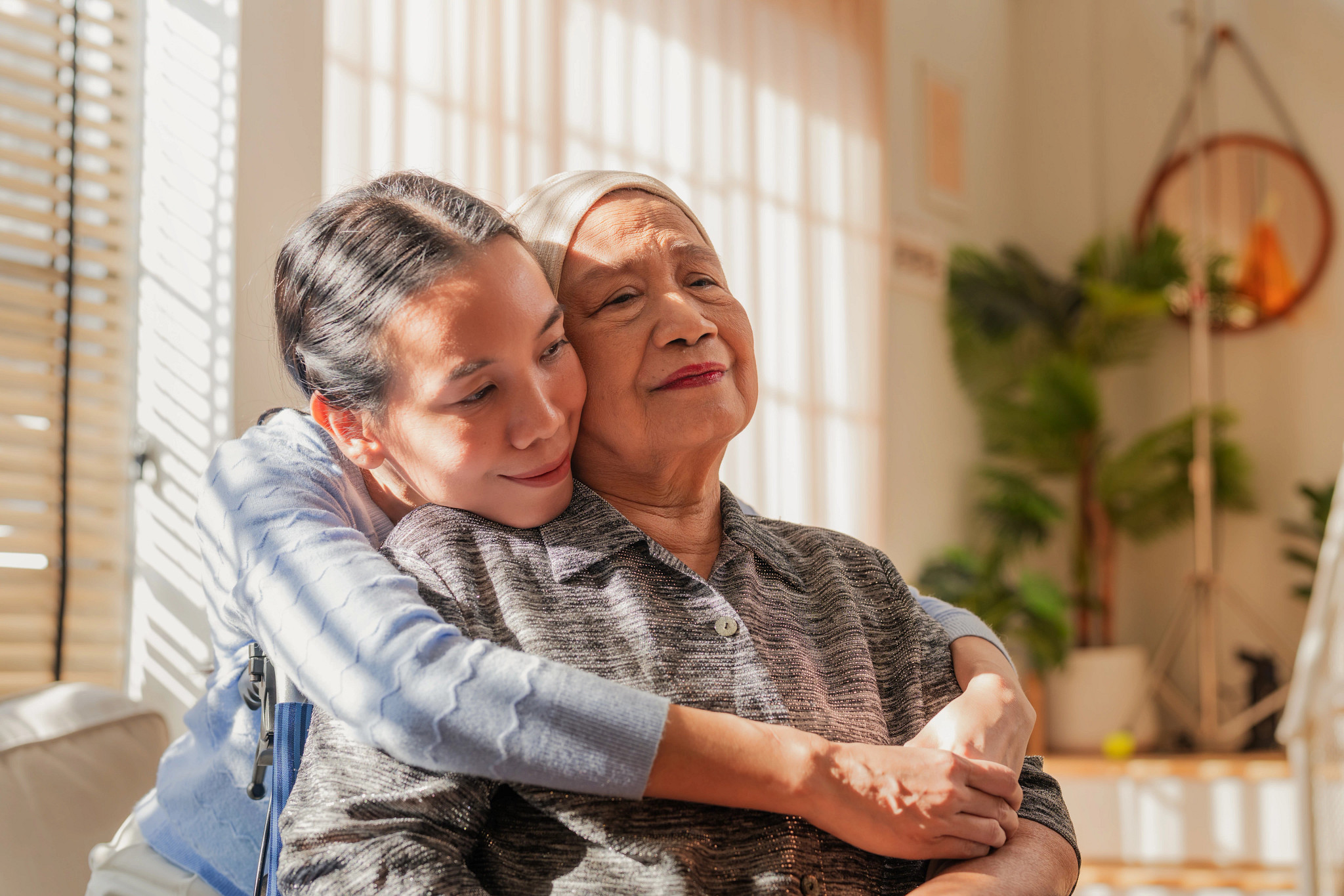 A woman sitting in a wheelchair as her daughter embraces her from behind