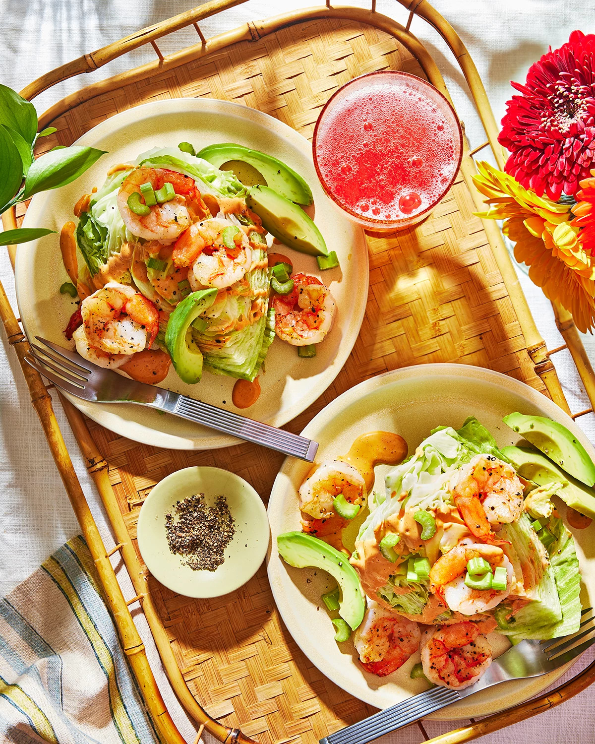 Shrimp and avocado wedge salads are plated and served on a woven bamboo tray alongside a refreshing pink beverage