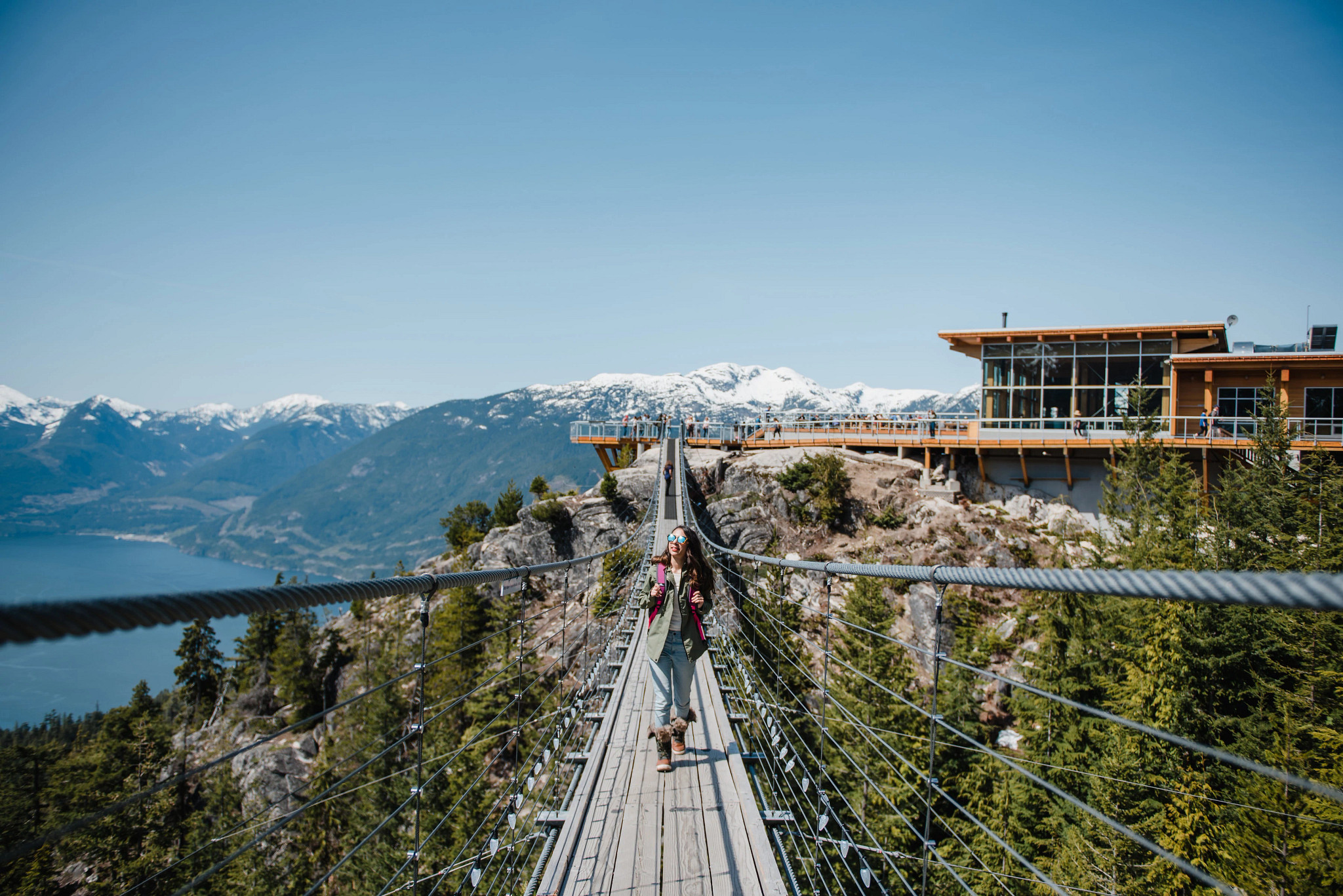people walking on a suspension bridge with a building and mountains in the background