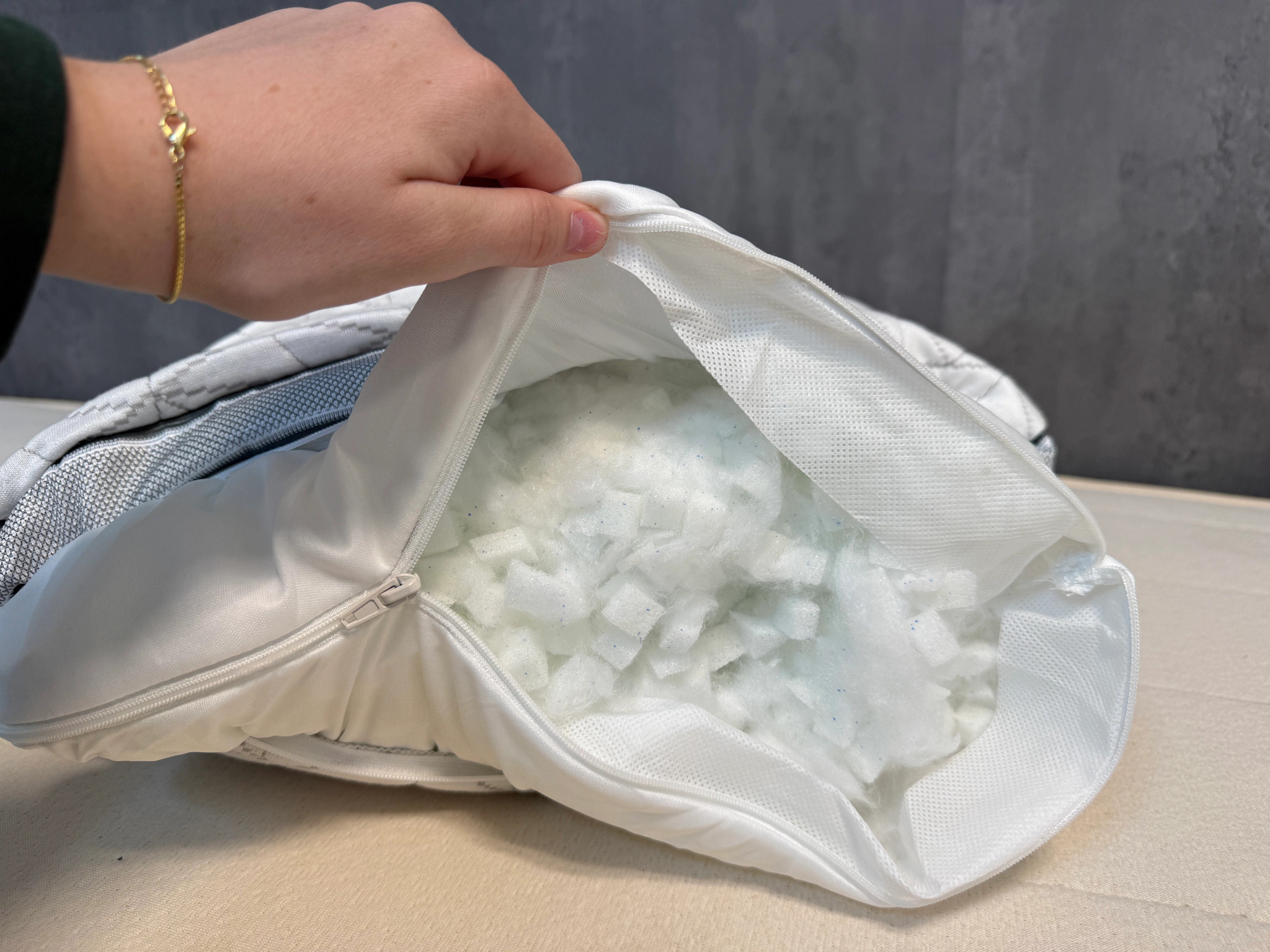 A hand holds open an unzipped Coop Eden Adjustable Pillow cover to show the fill inside