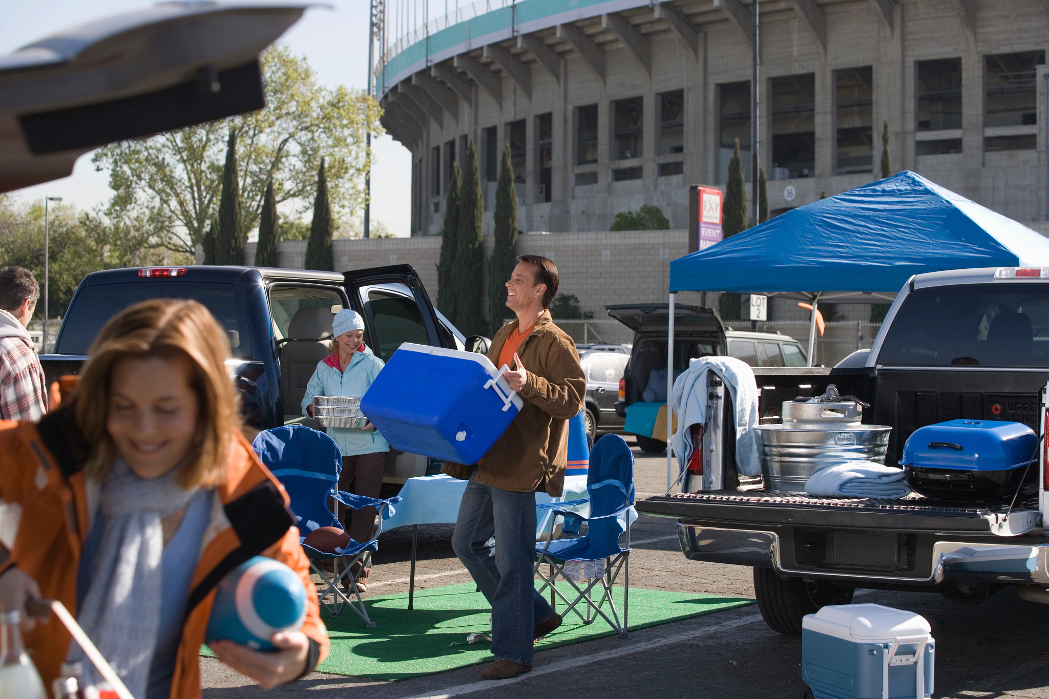 A photo shows tailgaters carrying coolers and cooking food