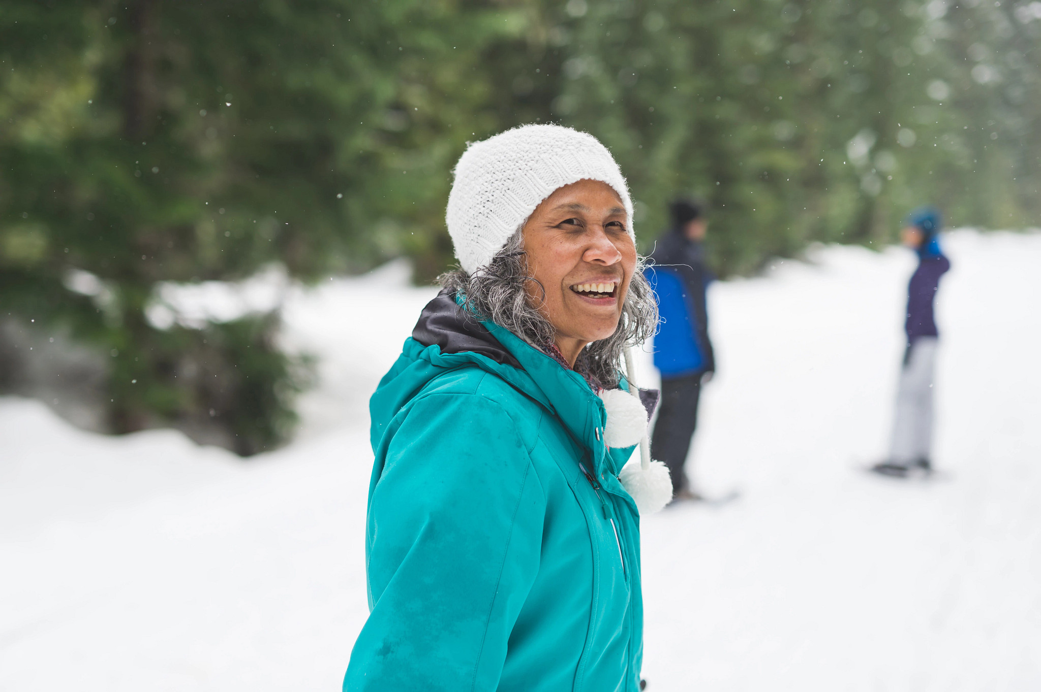 Smiling woman in a winter coat and white hat standing in a snowy forest