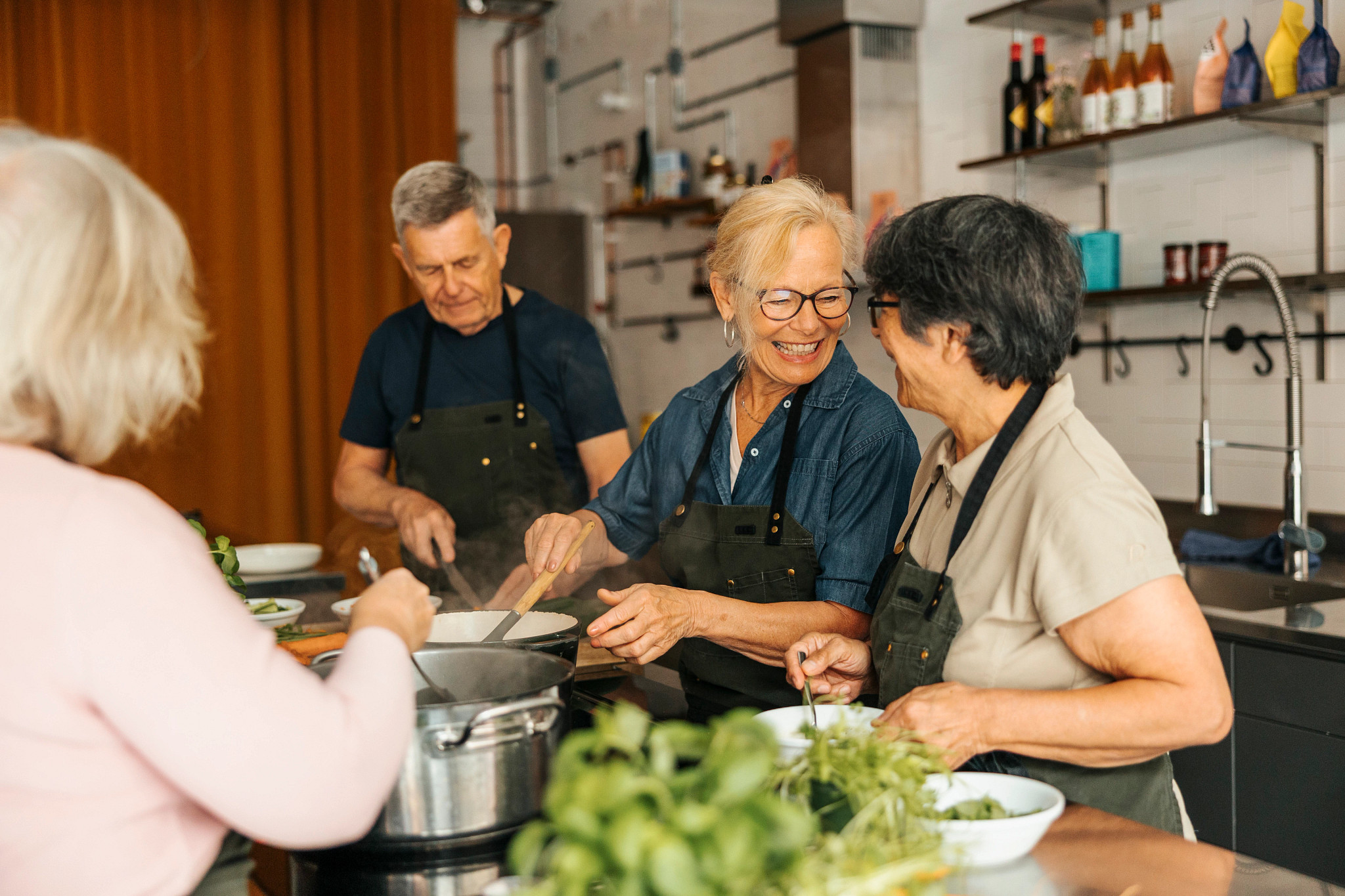 Three women and one man cooking together in a class in a commercial kitchen