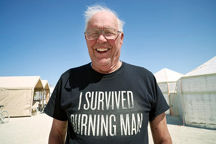 a man smiling and wearing a Burning Man shirt