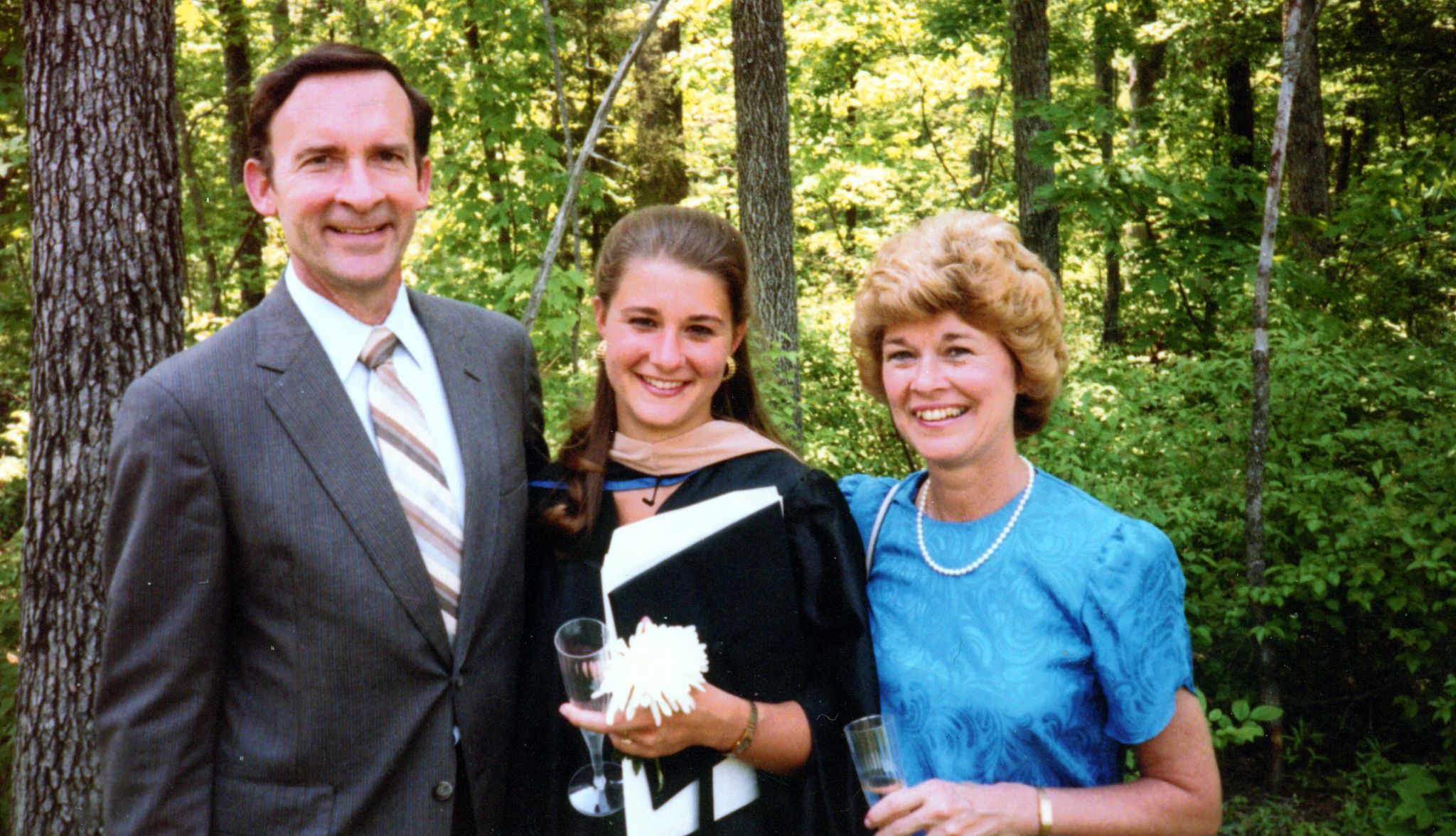 Melinda French Gates with her parents melinda in a black graduation gown, surrounded by her mother and father
