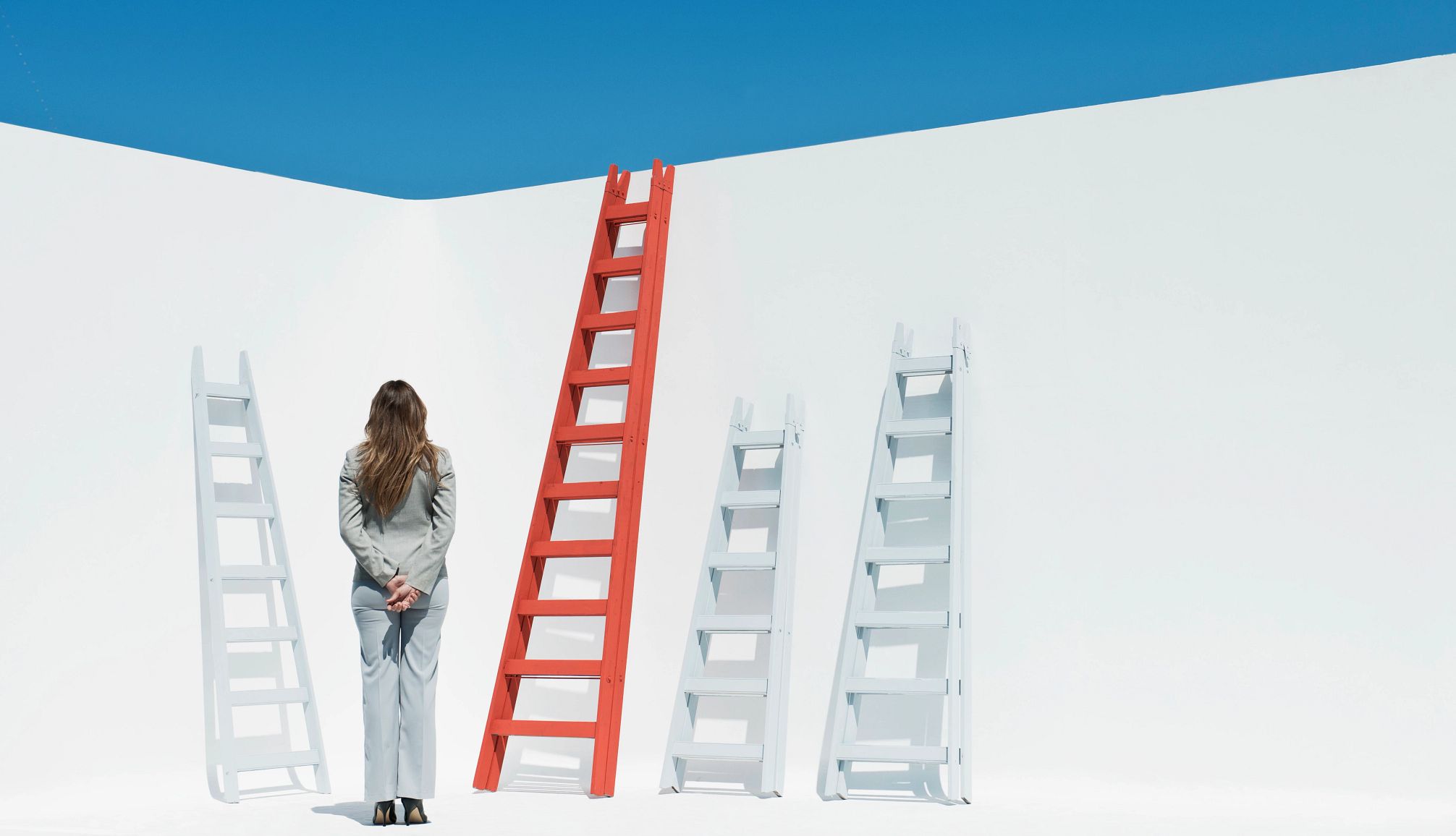 Mental Job Barriers a woman looking at three white ladders and one red ladder