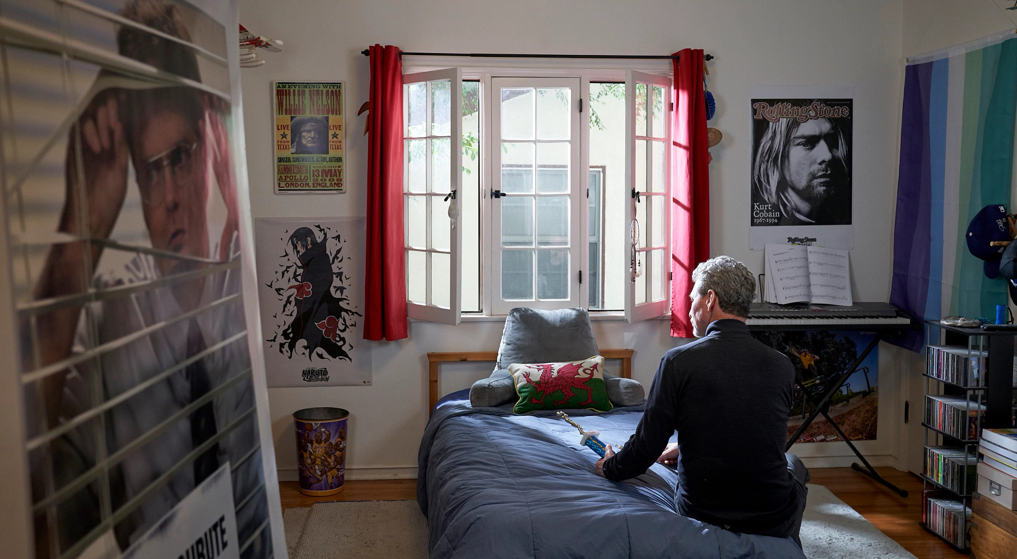 a photo shows a dad sitting on his son’s bed, looking forlornly at sports trophy. On the wall are posters of Kurt Cobain and the office tv show