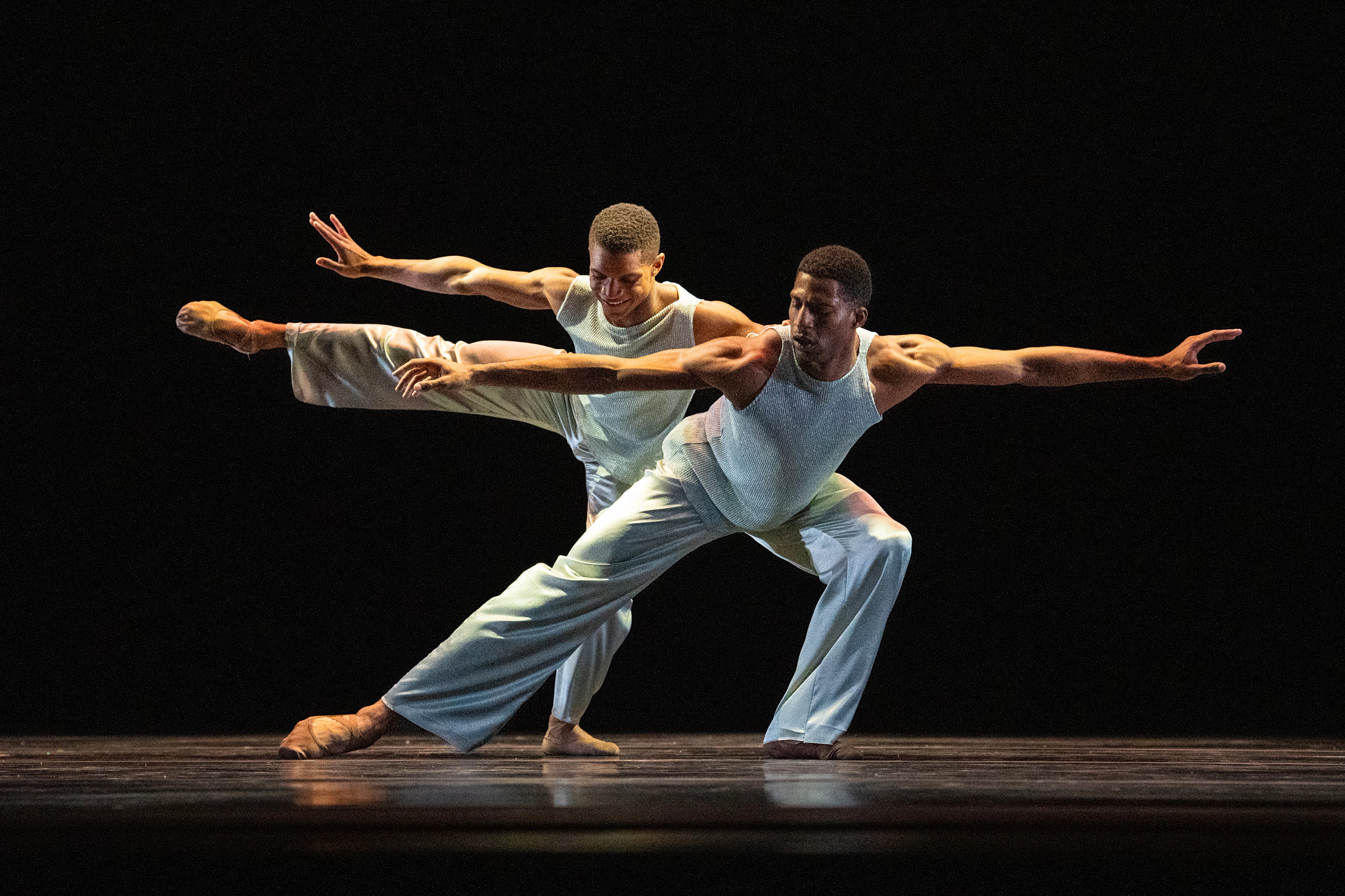 Two dancers perform a contemporary dance duet onstage with synchronized movements and athletic poses.