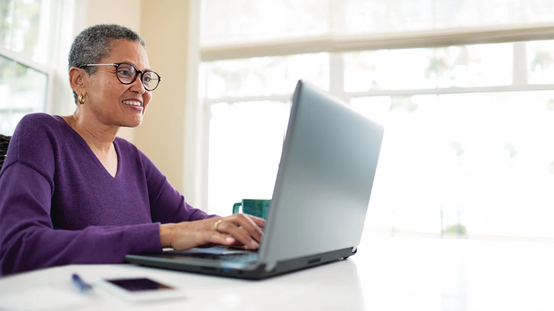 older woman typing on laptop smiling with purple shirt