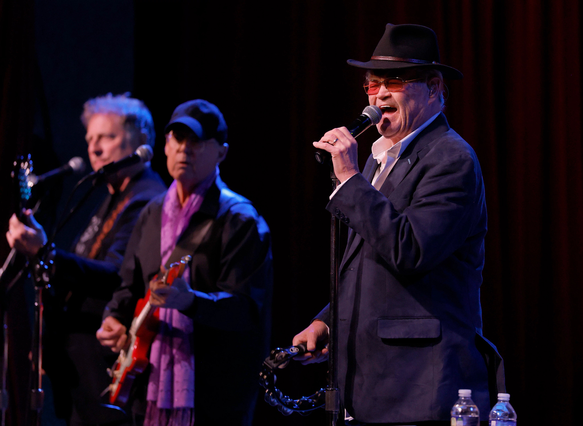 Micky Dolenz performing onstage, with band members in the background