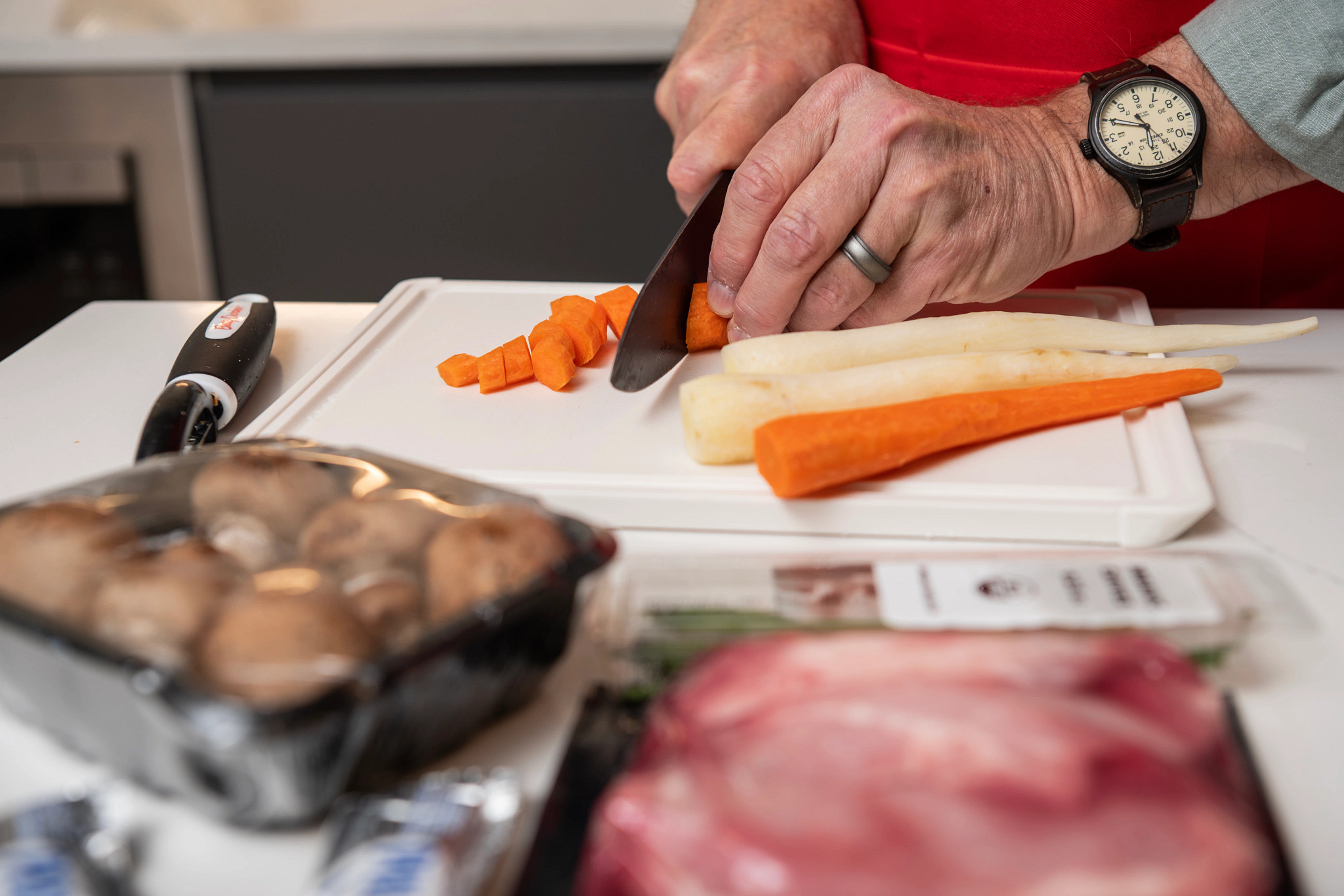  A man cutting up a carrot on a white cutting board