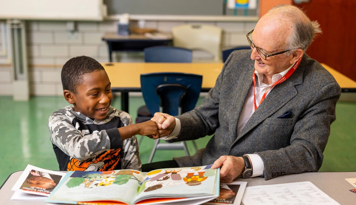 Young boy fist bumping older man with an open book in front of them