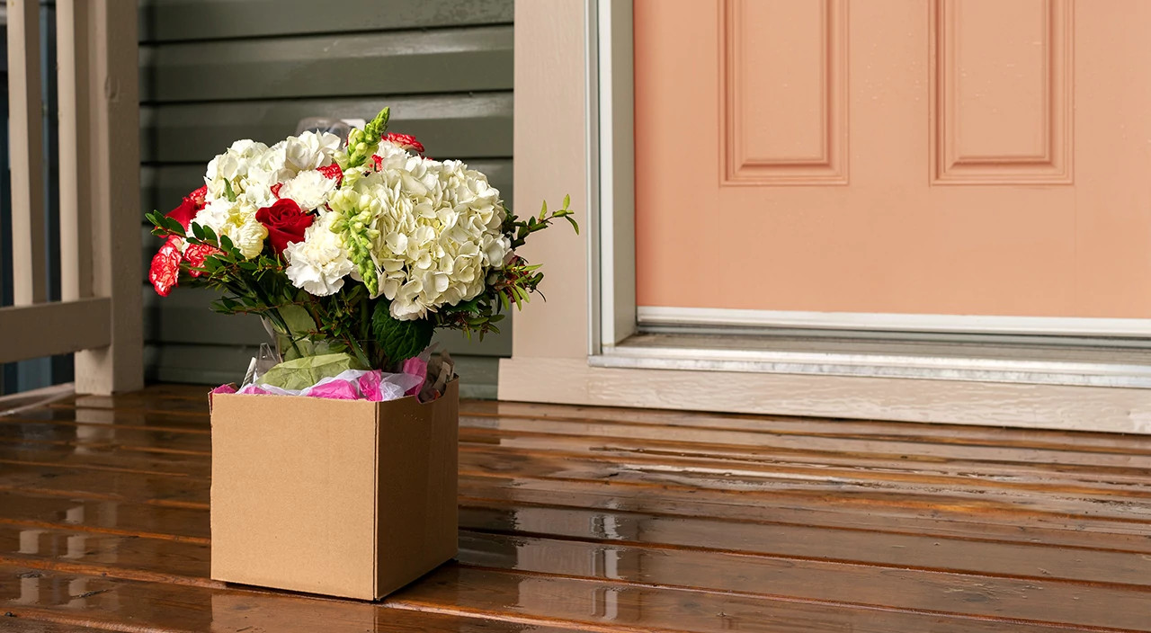A box with a flower bouquet on a front porch in front of the door