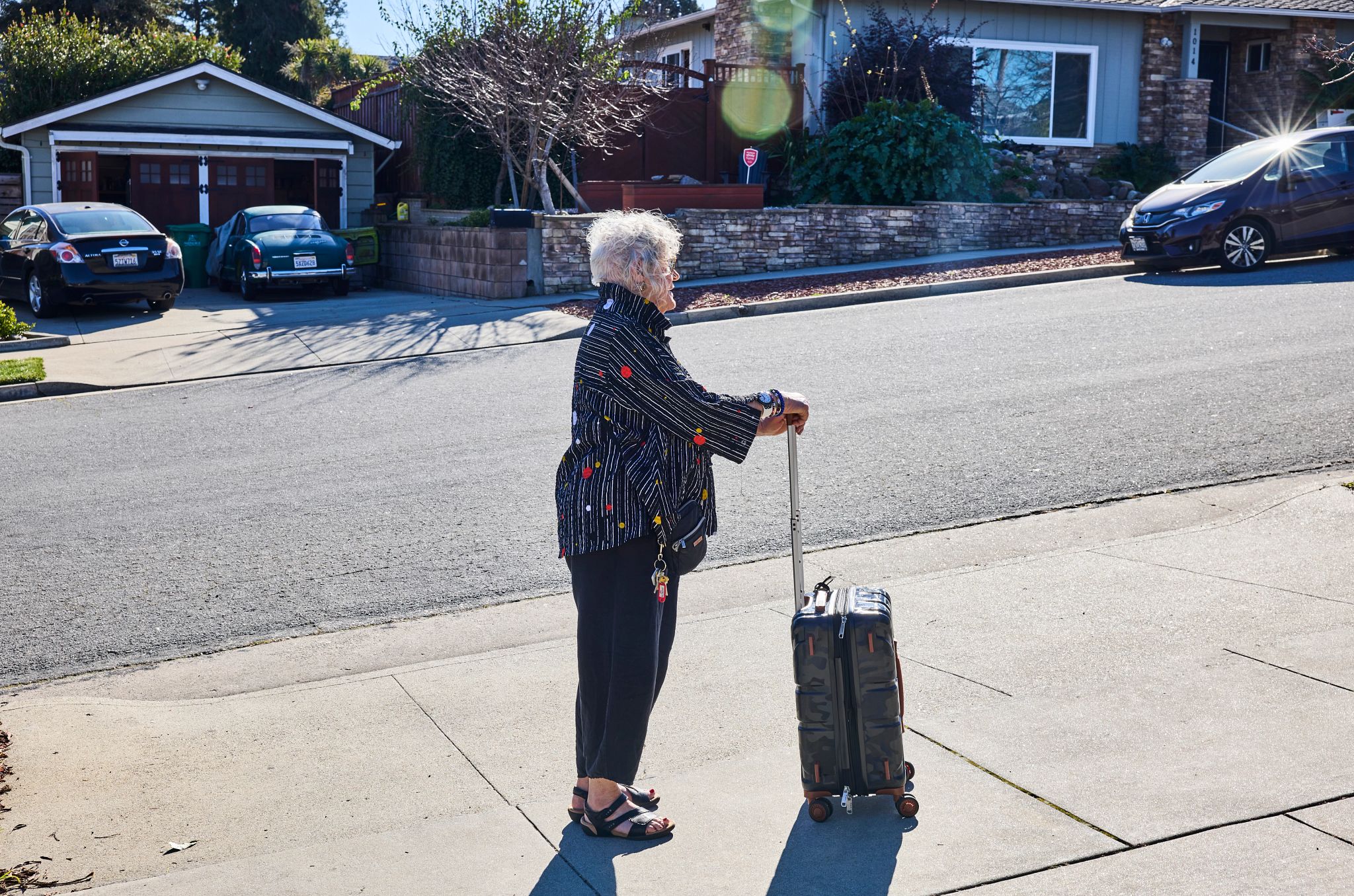My Experience With Ride-Share Apps jane gregorius stands on the sidewalk with a rolling suitcase while she waits to be picked up