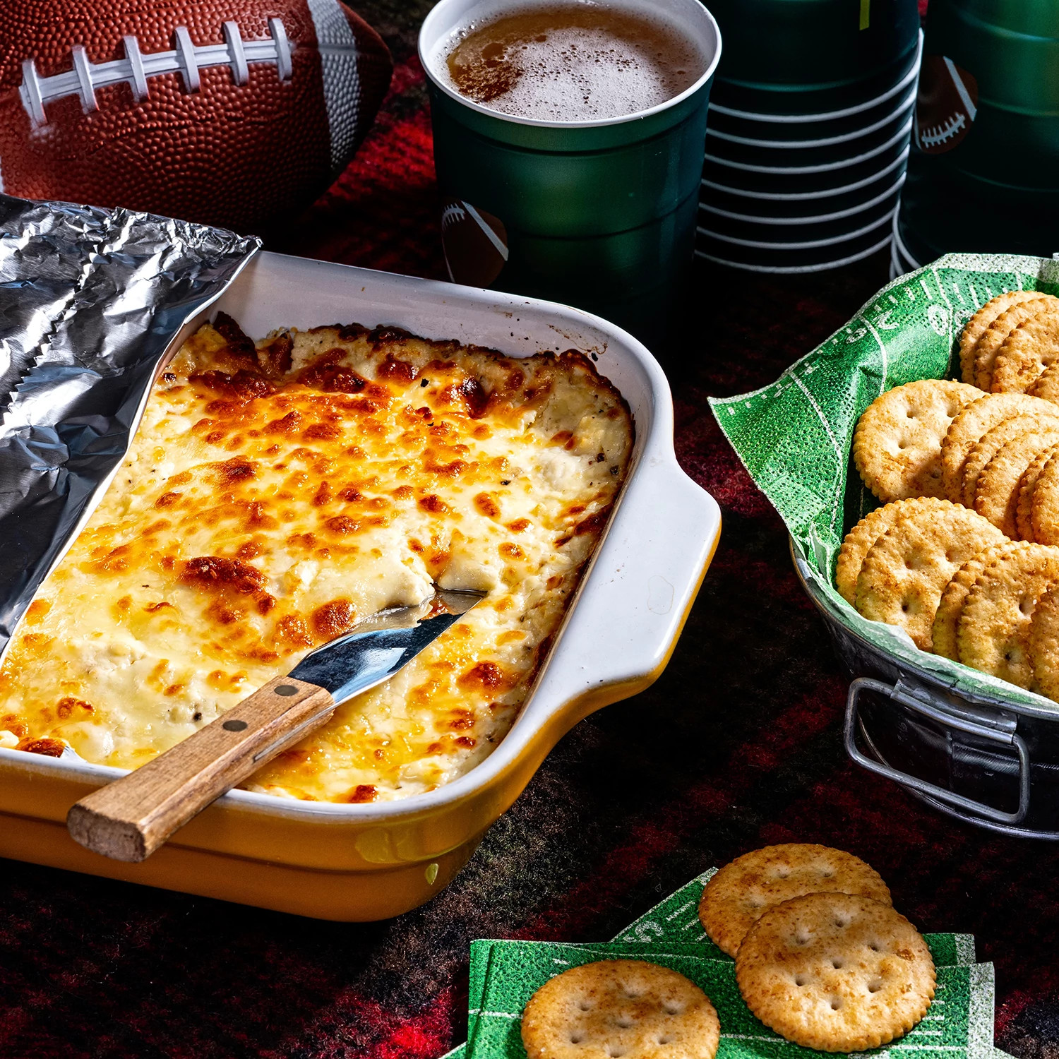 Golden baked cheese dip in a white casserole dish surrounded by crackers and party snacks.