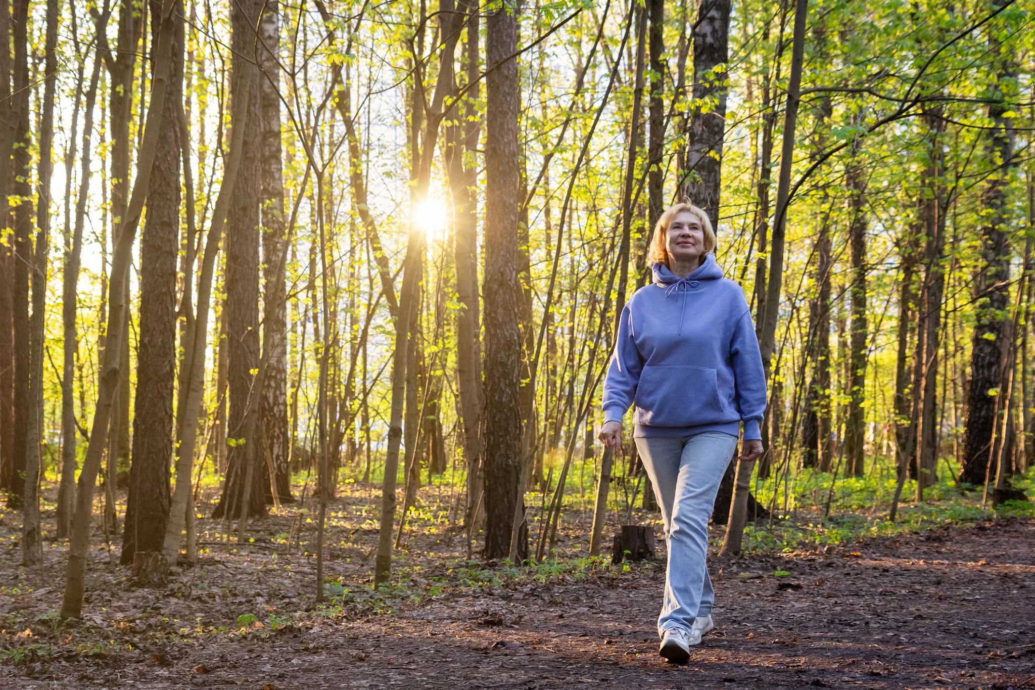 Woman walking in the woods with the sun peeking through the tall trees.