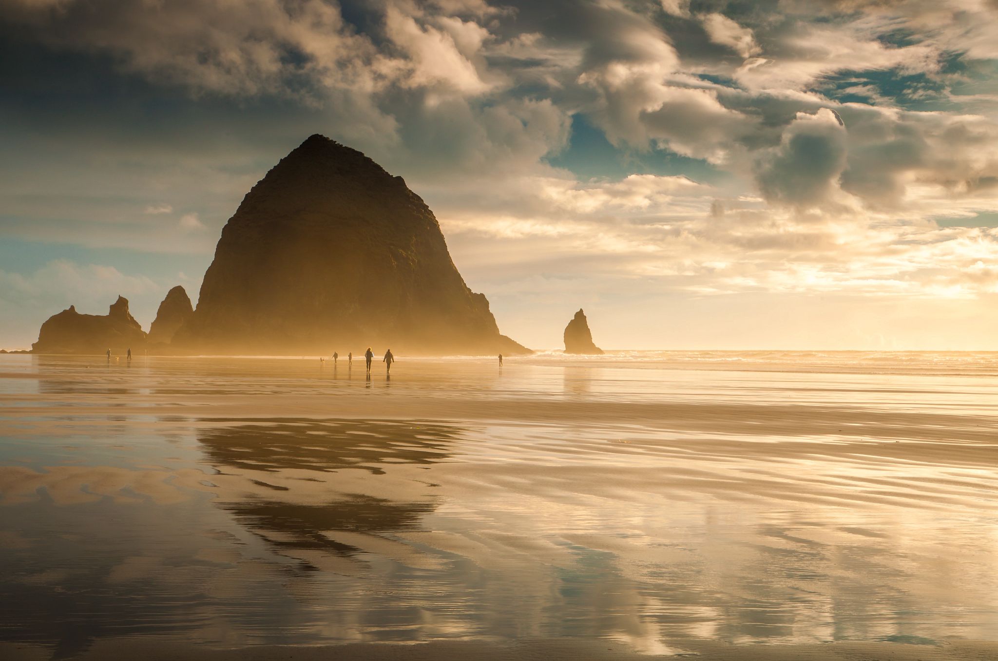 America’s Most Unique Beaches beachgoers walking at Oregon’s Cannon Beach with Haystack Rock in the distance