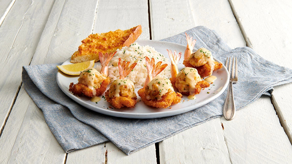 wood table with gray napkin white plate stuffed shrimp, fried fish, rice and lemon