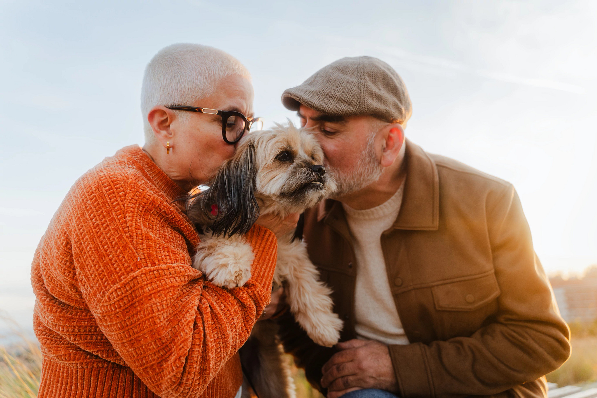 a photo shows two older adults kissing their dog