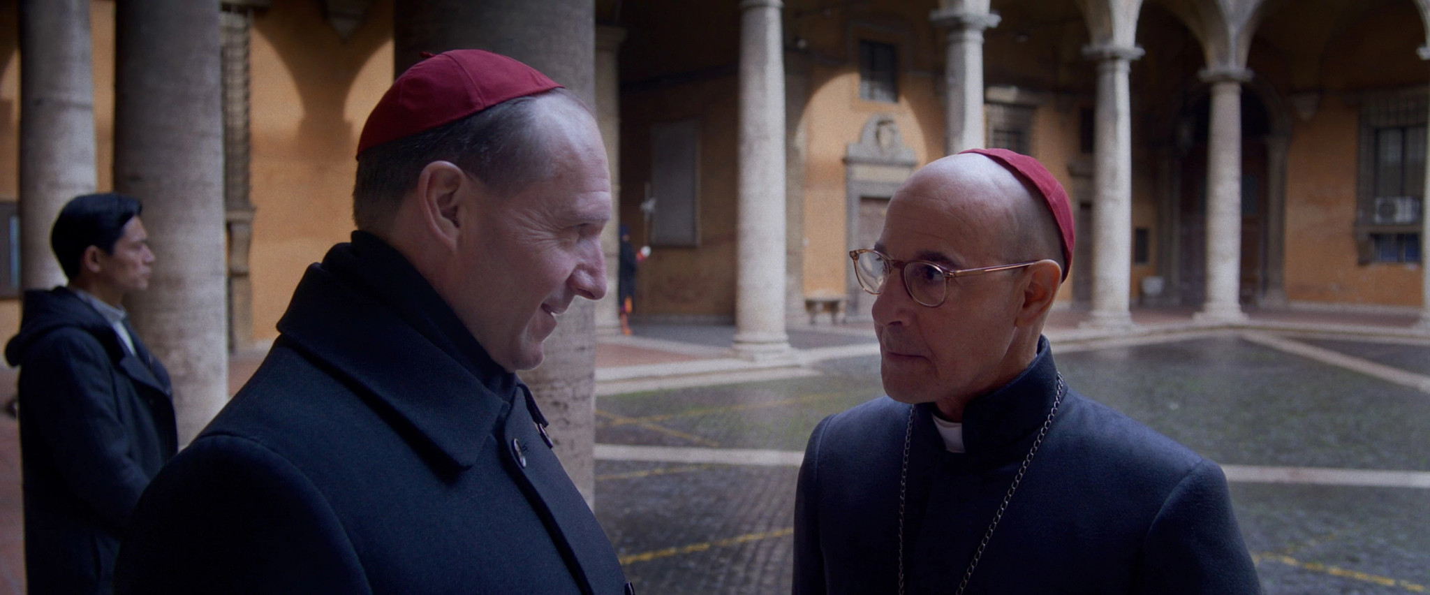 Ralph Fiennes with Stanley Tucci each wearing a zucchetto in a still from Conclave