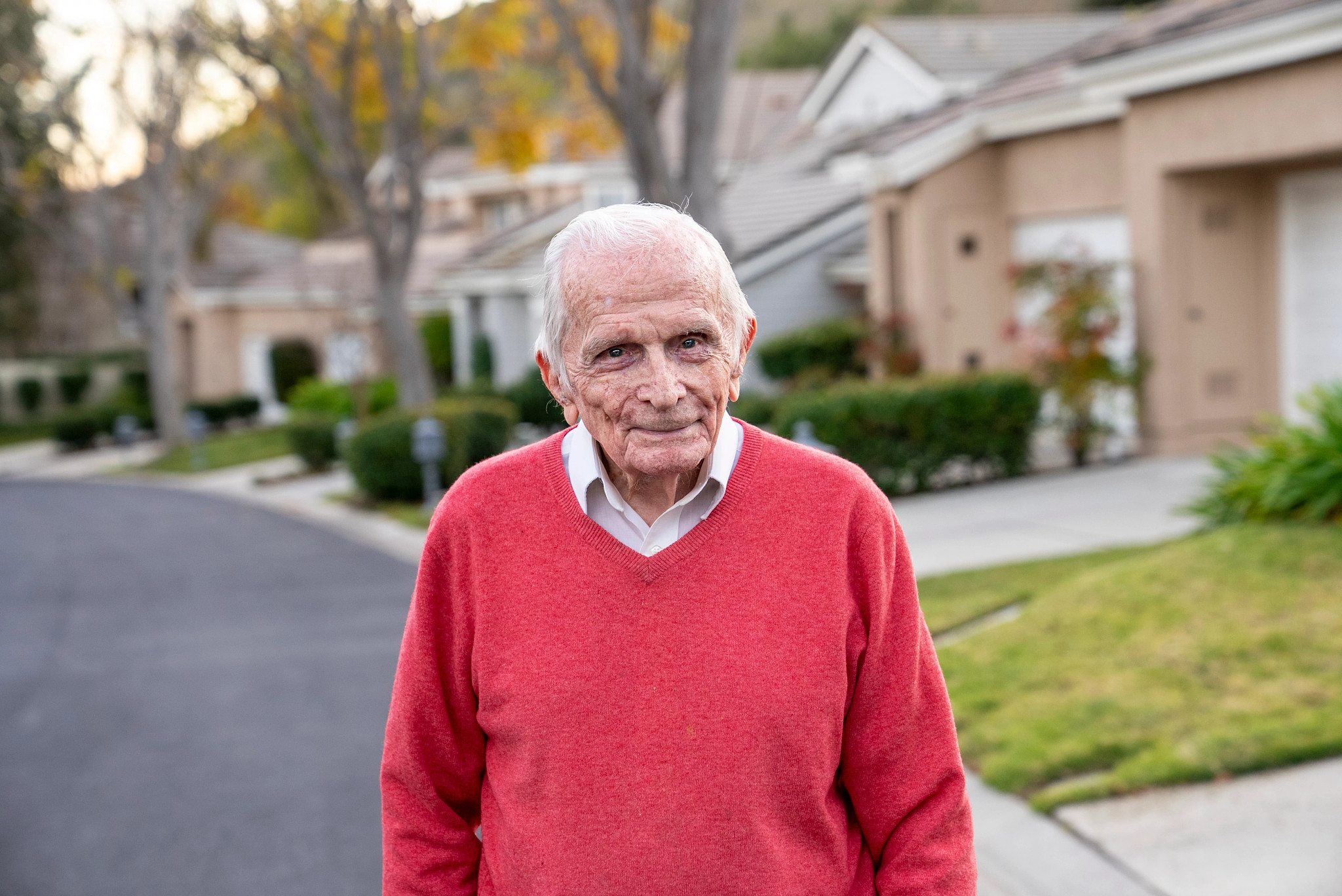 Jack Moran standing outside in red sweater in front of houses