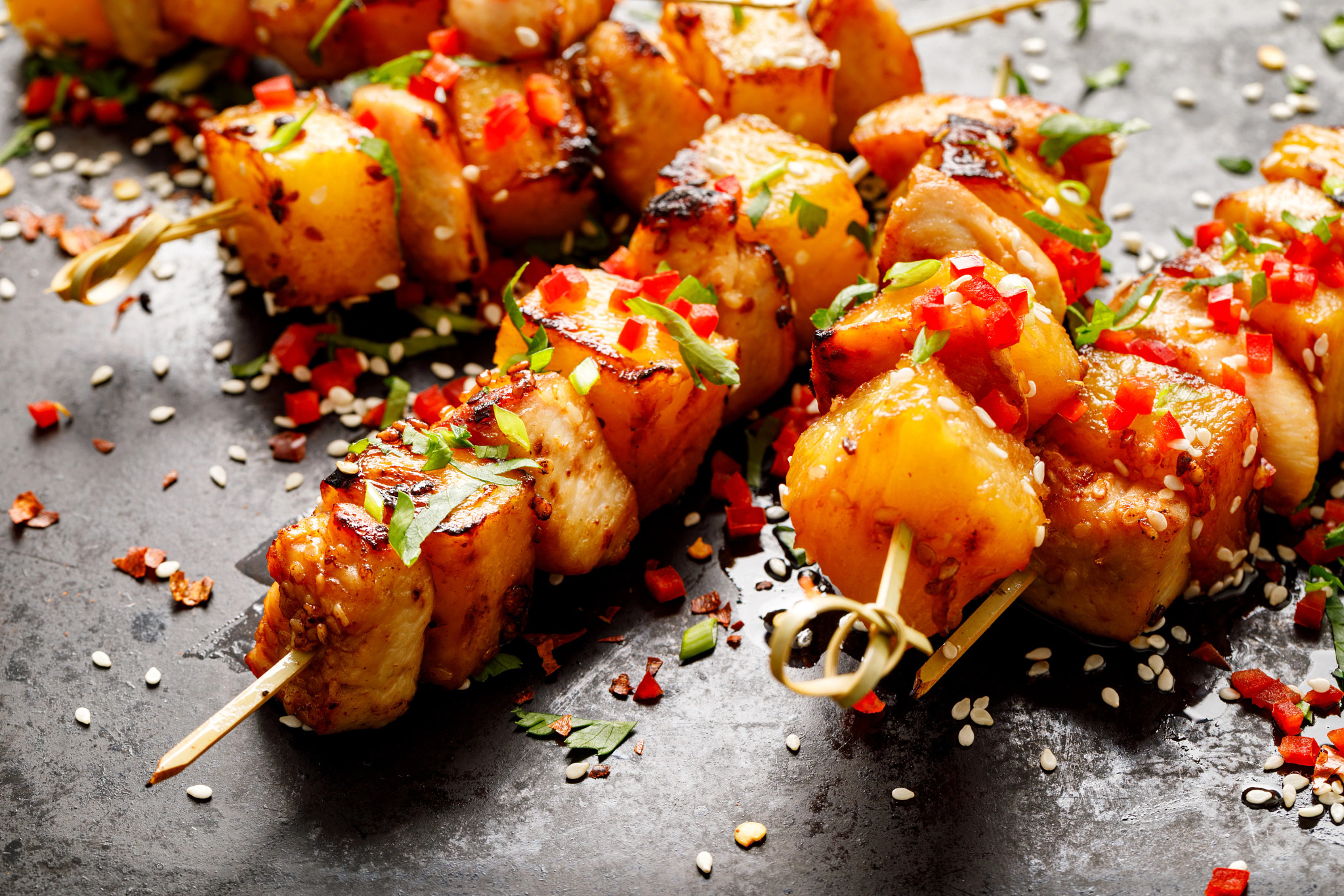 Yuzu kosho chicken skewers with grilled pineapple are pictured. The skewers are garnished with sesame seeds.