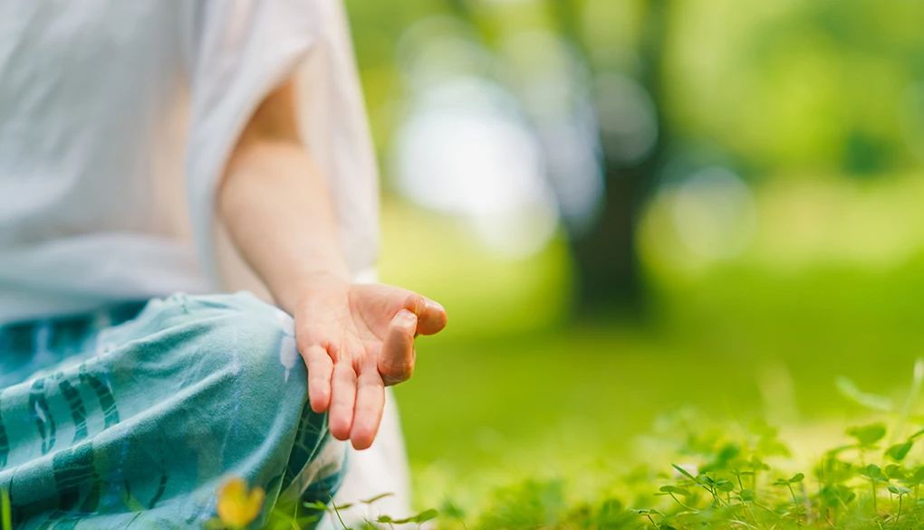 Meditation may help amplify your experience of optimism A close-up view of a woman's hand while in a yoga position in nature