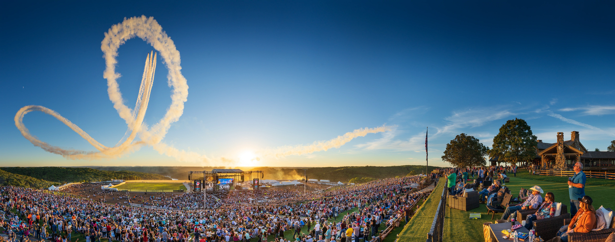 a large crowd watches an airshow at a concert venue