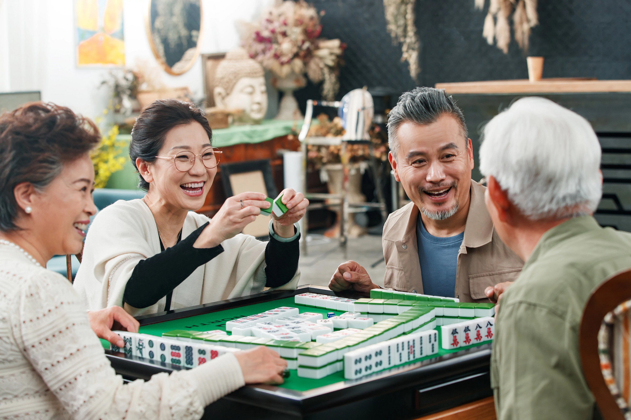Two men and two women sitting around a table playing mahjong