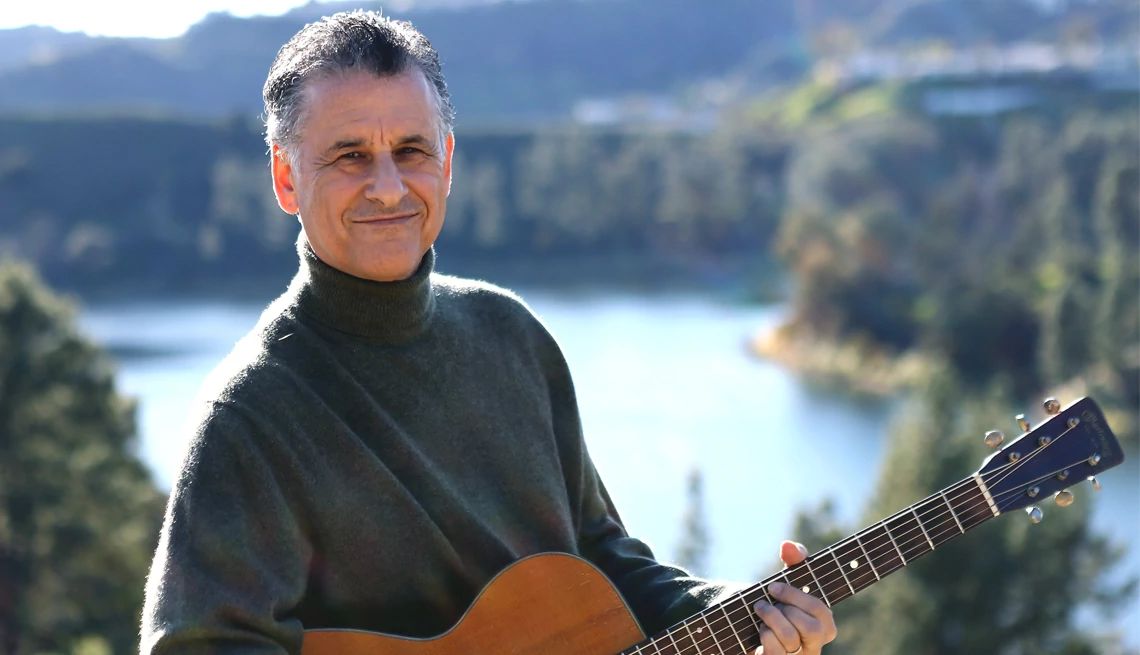 Playing an instrument may be good for brain health Daniel Levitin holding a guitar with a lake surrounded by trees in the background