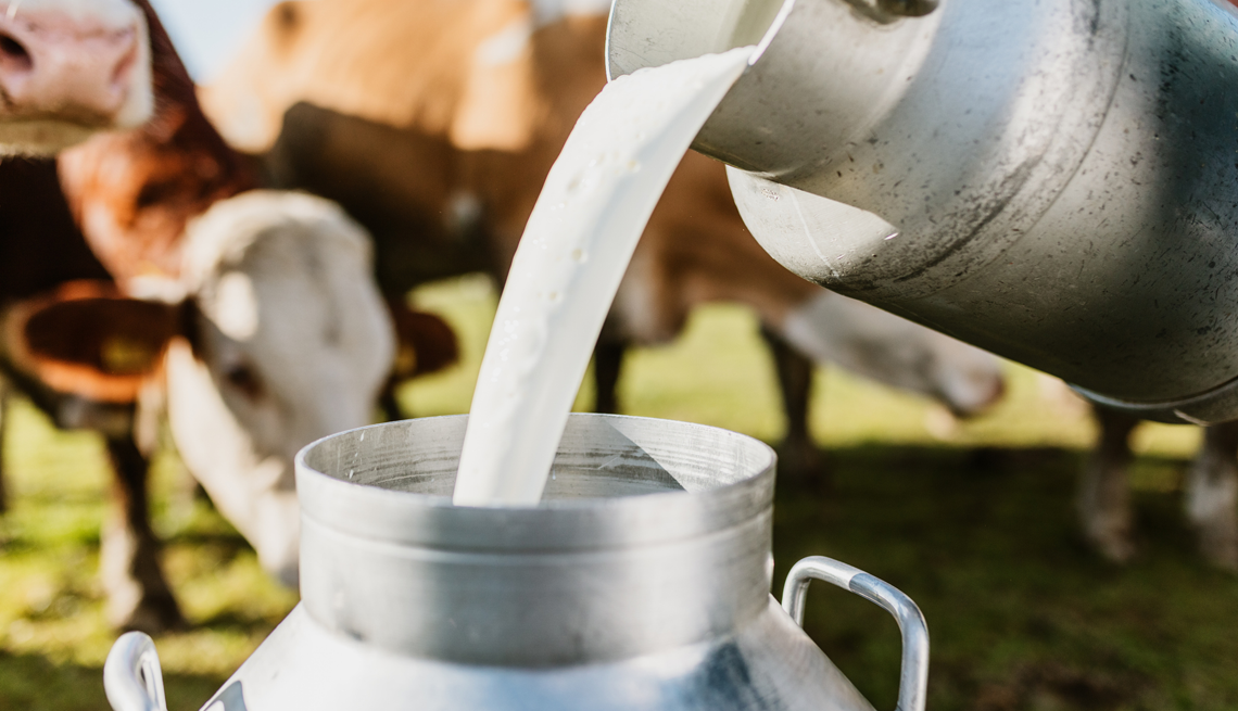 milk from a jug being poured into a tin pitcher