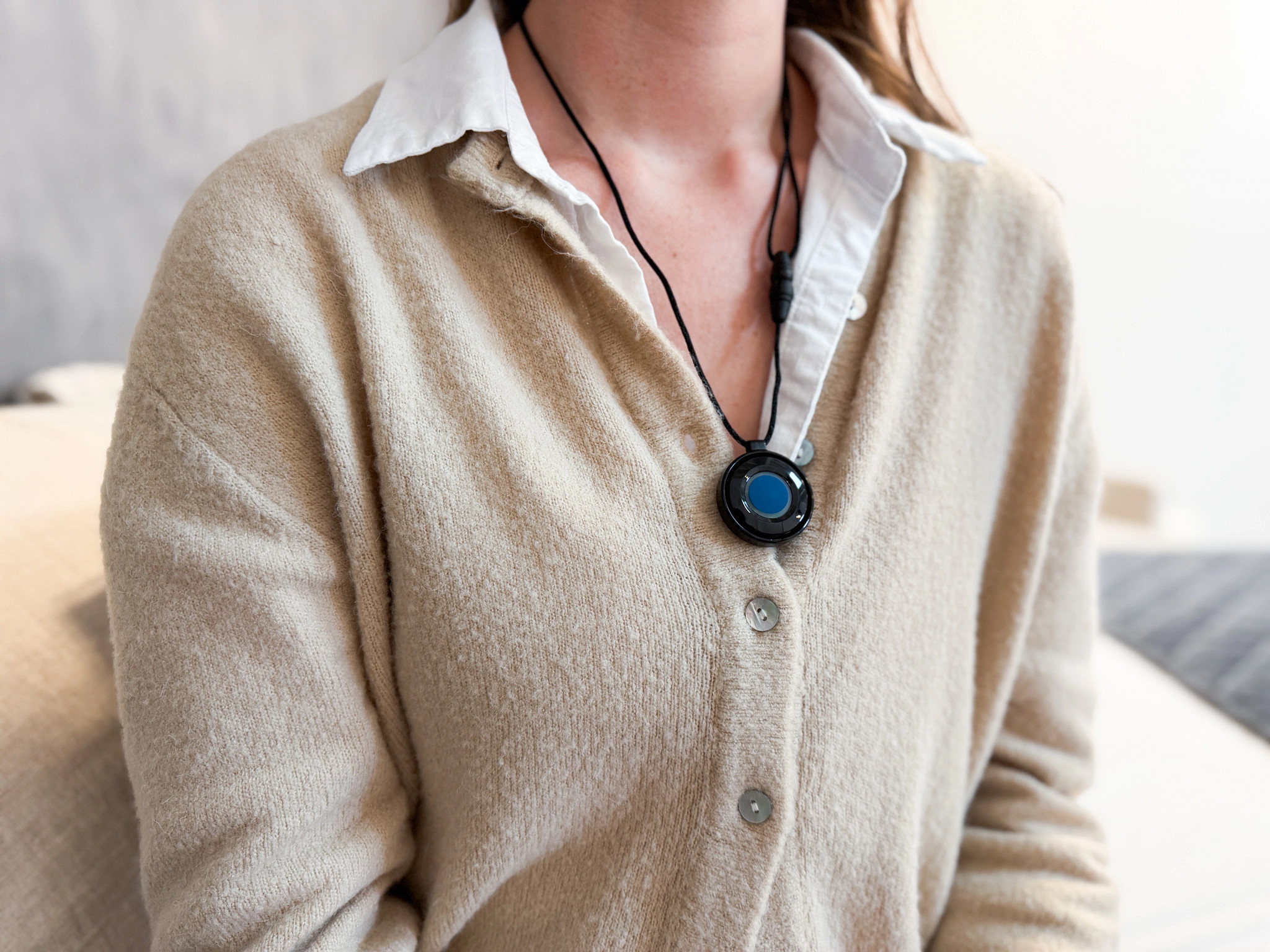 Woman wears a brown cardigan and a help button on a necklace.