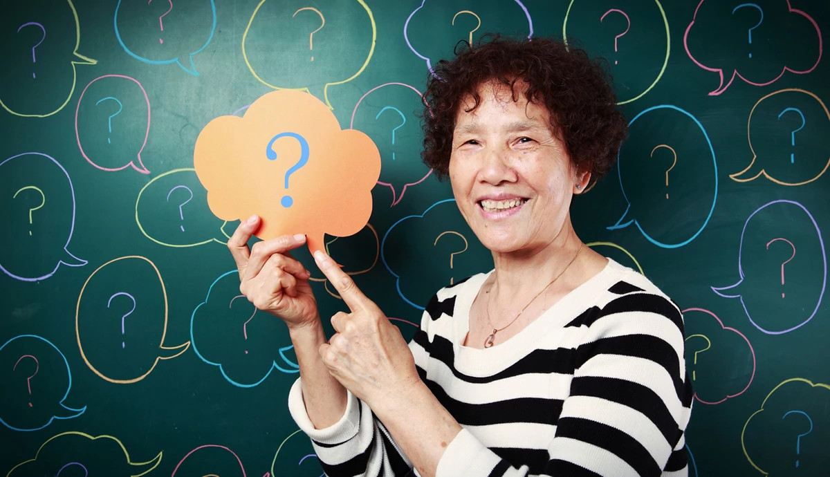 A smiling woman points to a sign with a question mark.
