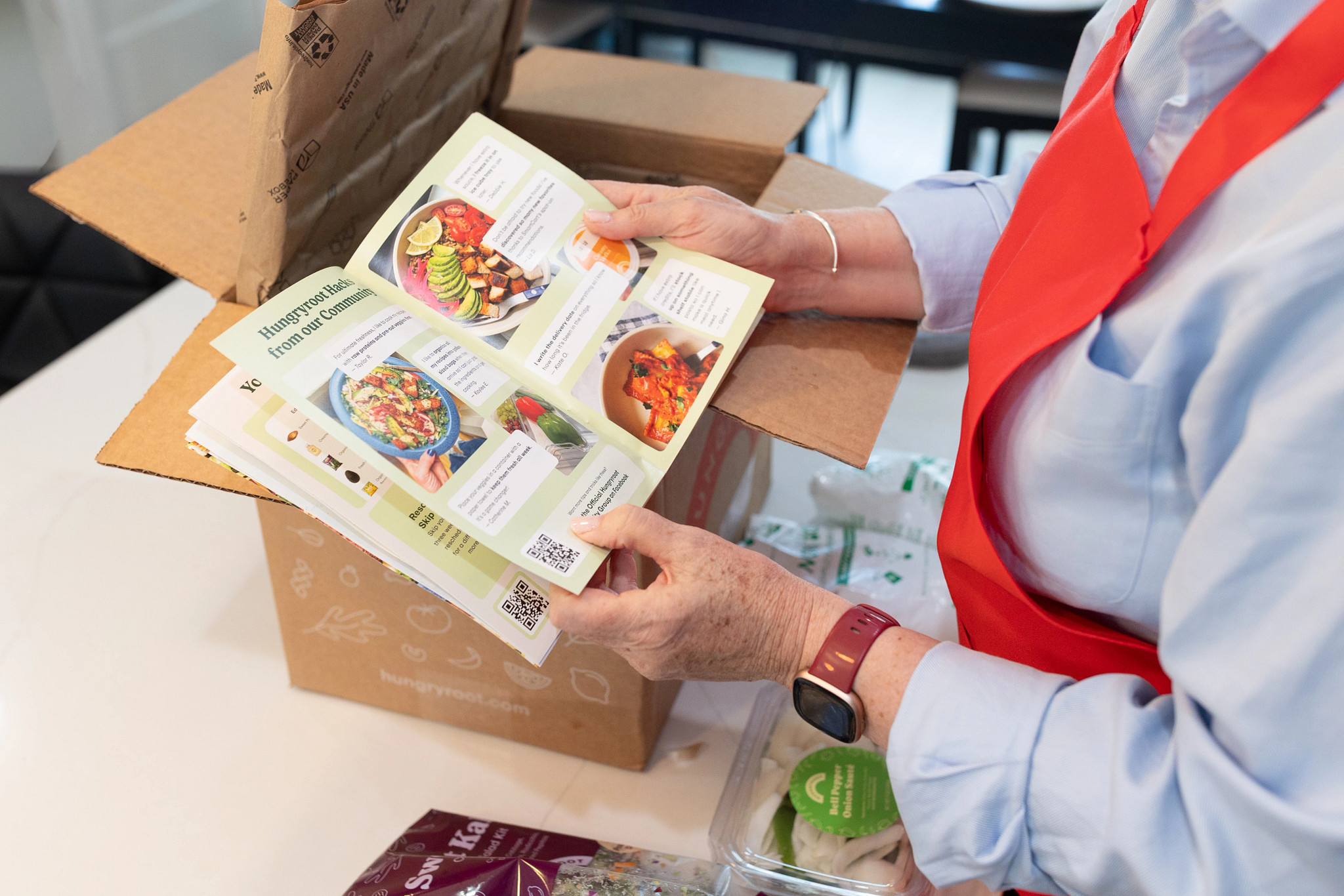 A person holding open an informational Hungryroot packet over the meal kit delivery box 