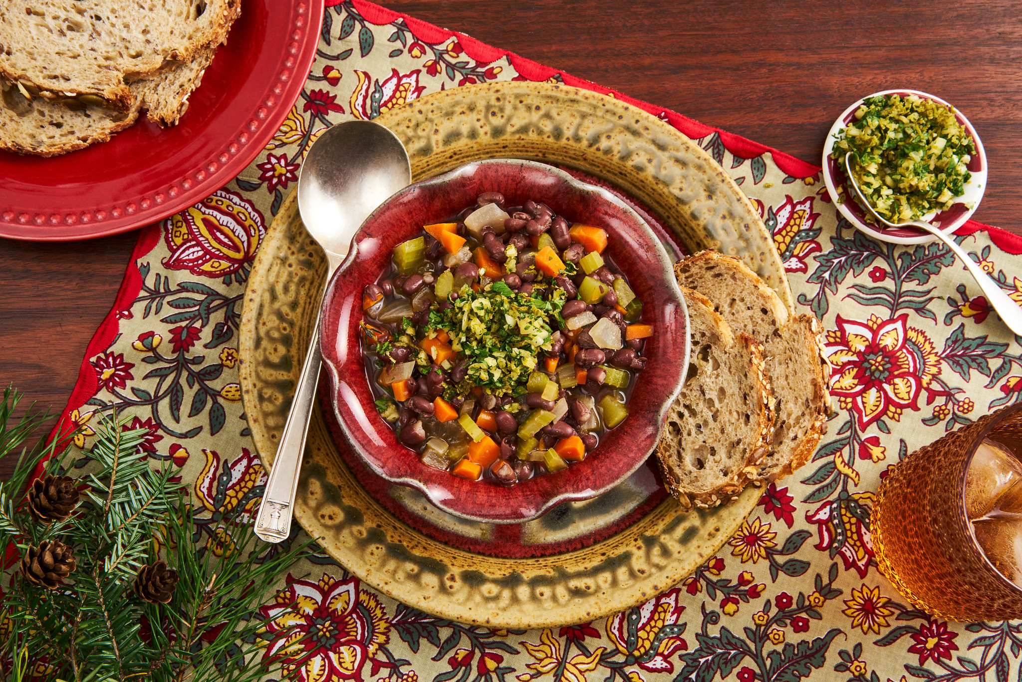 Hearty holiday bean soup with carrots and herbs served in a red ceramic bowl with crusty bread on a festive table