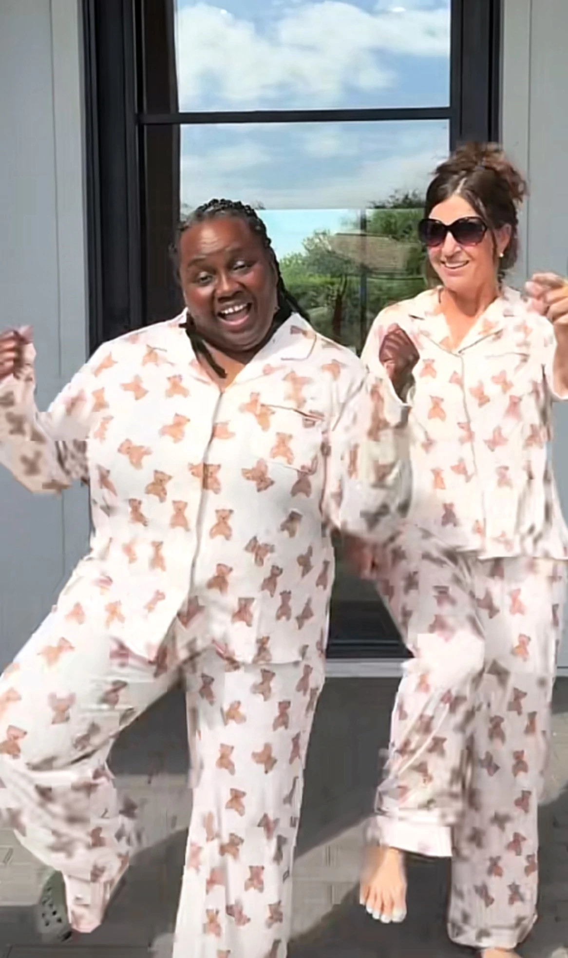 Gramfluencers wearing matching patterned pajamas outdoors near a modern window posing playfully