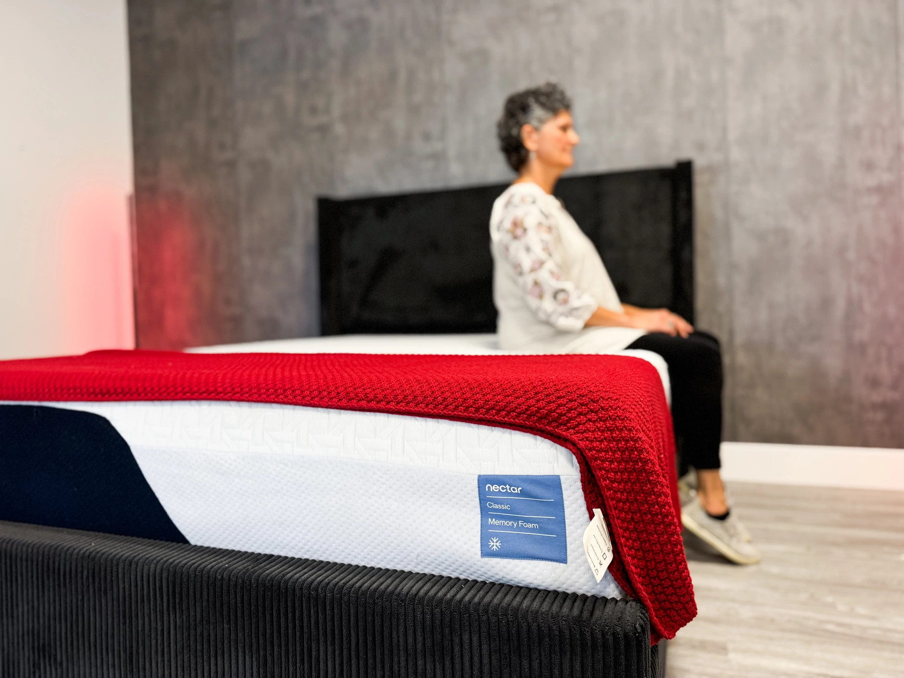 A woman sits on the edge of the Nectar Classic Memory Foam mattress