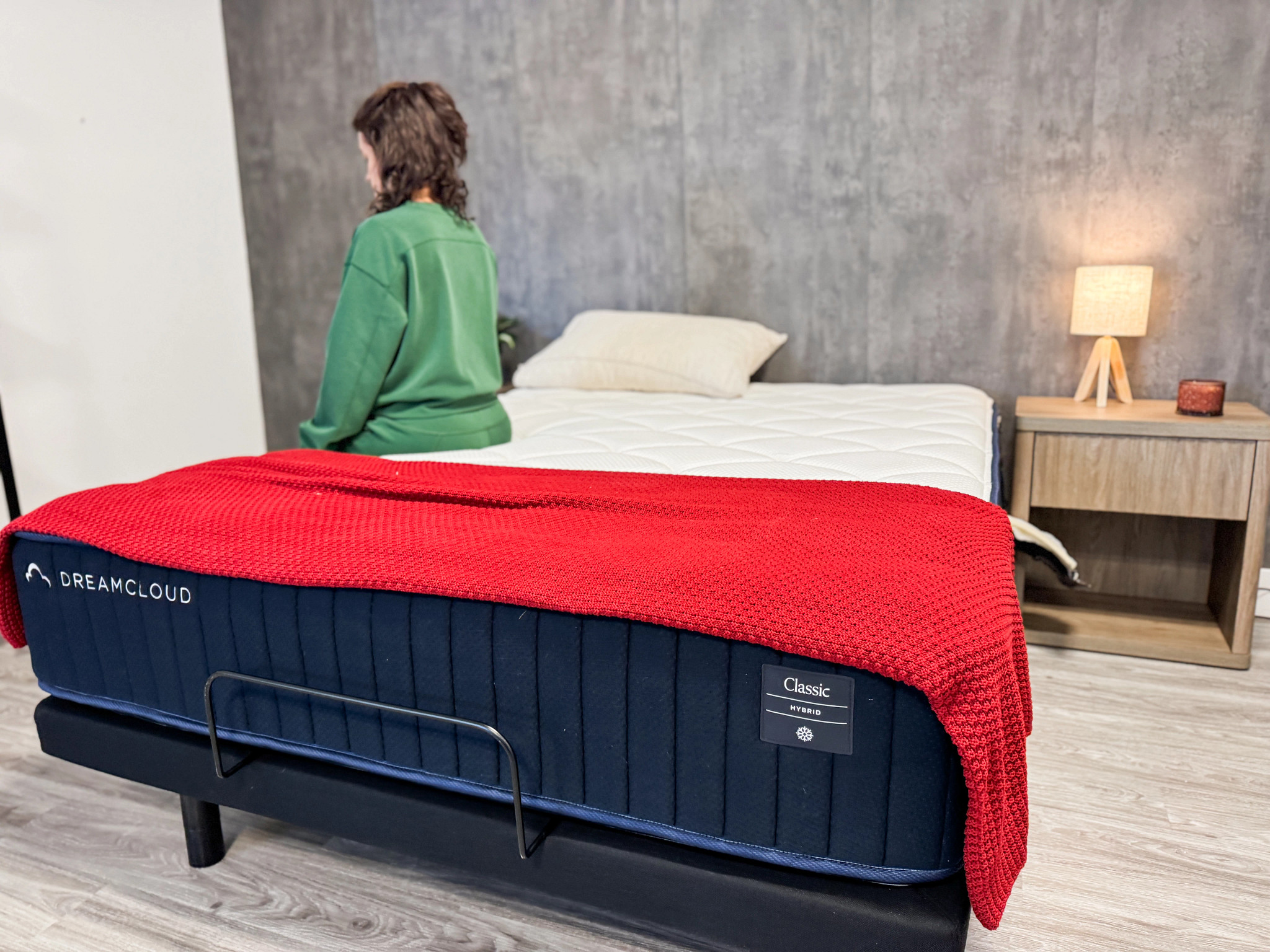 A person sits on the edge of the DreamCloud Classic Hybrid mattress in a bedroom