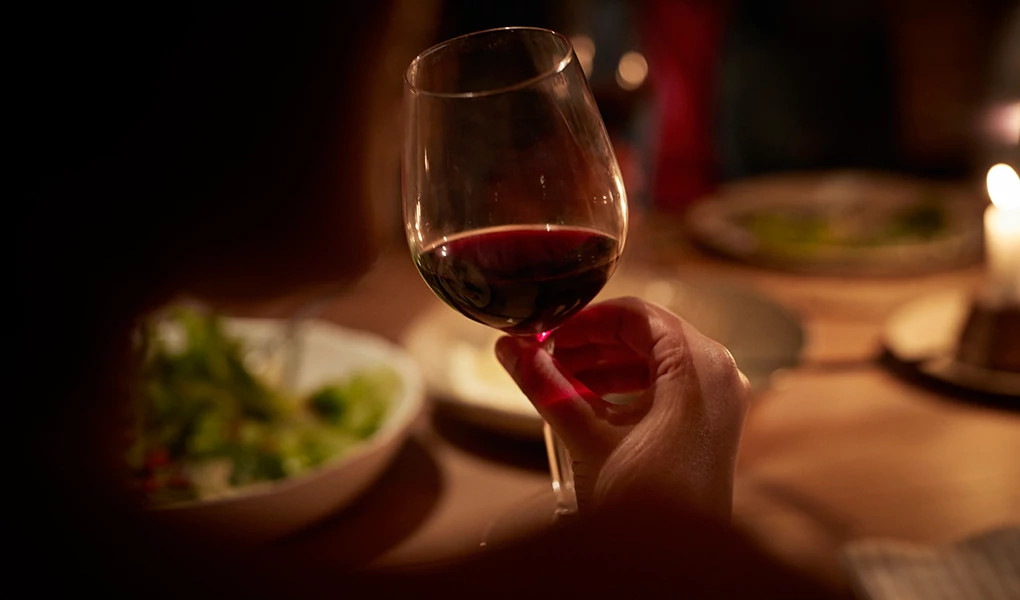 A hand holding a glass of wine at a dinner table