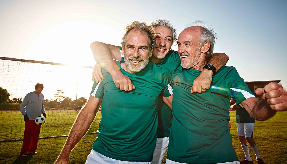 Group of mature men hugging after a soccer match wearing green jerseys, goalie in the background