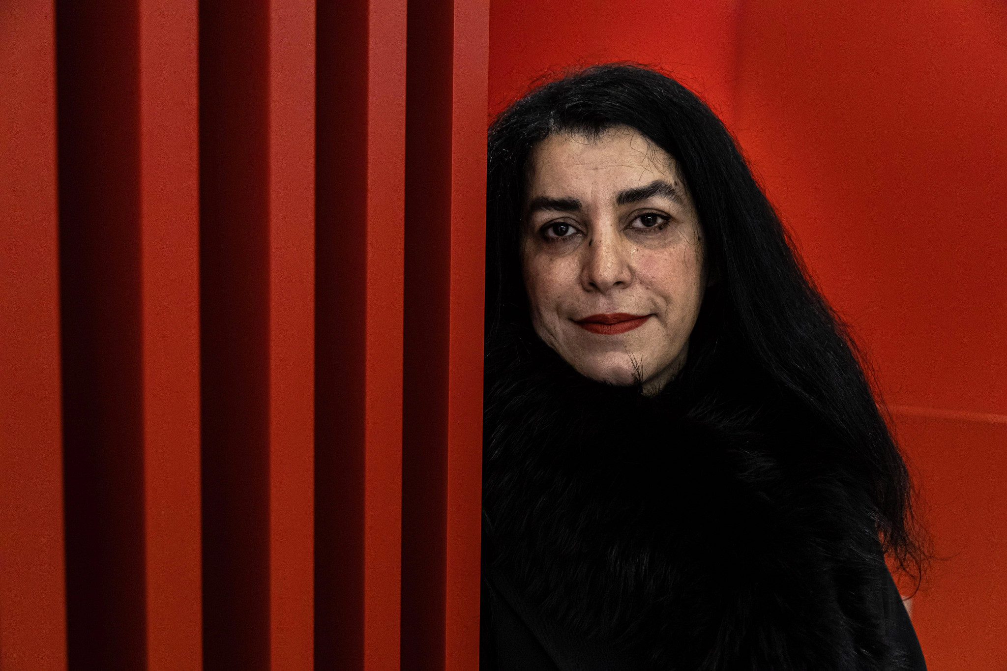 a head shot of marjane satrapi against a red background